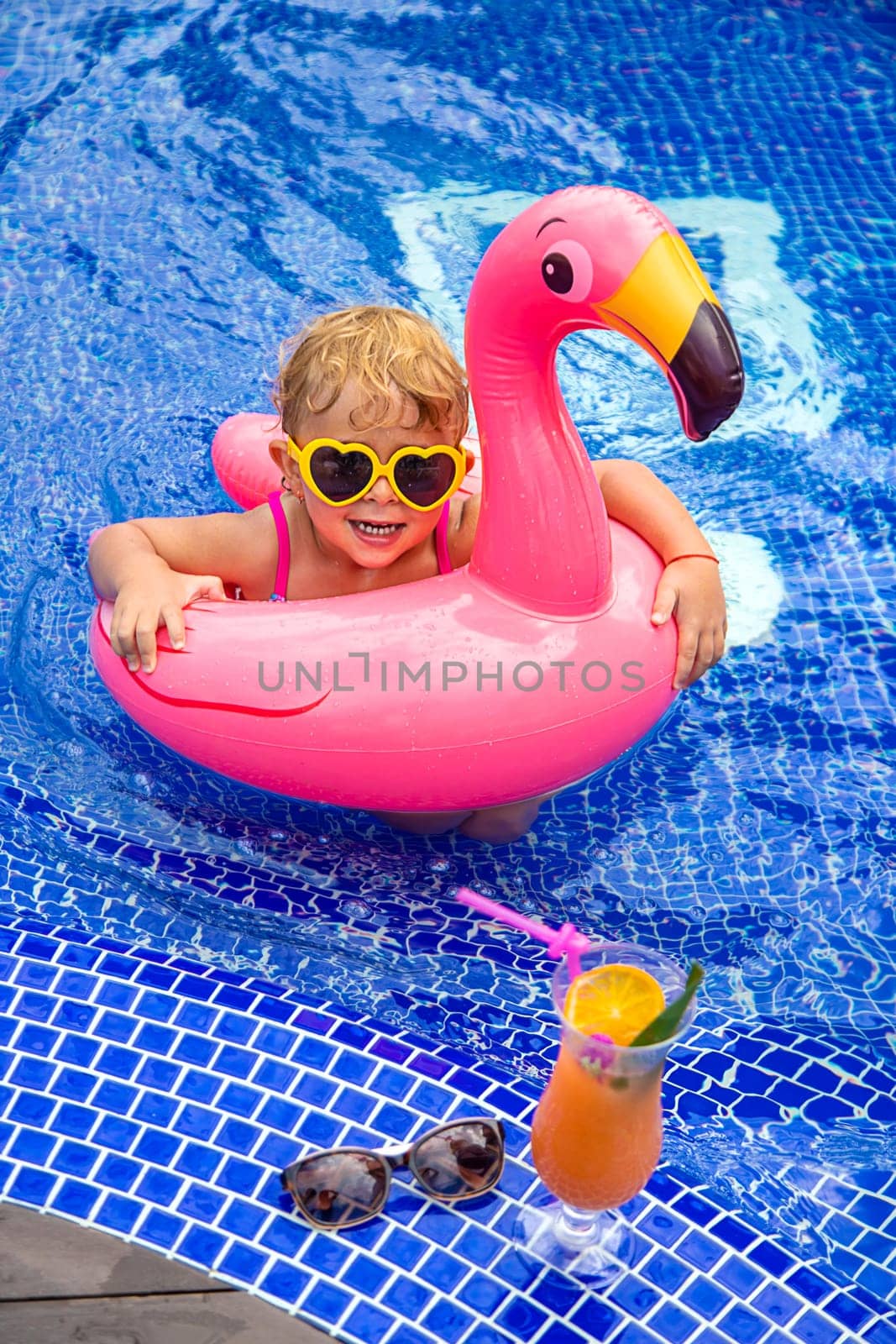 A child in a pool swims in a circle of flamingos. Selective focus. by yanadjana
