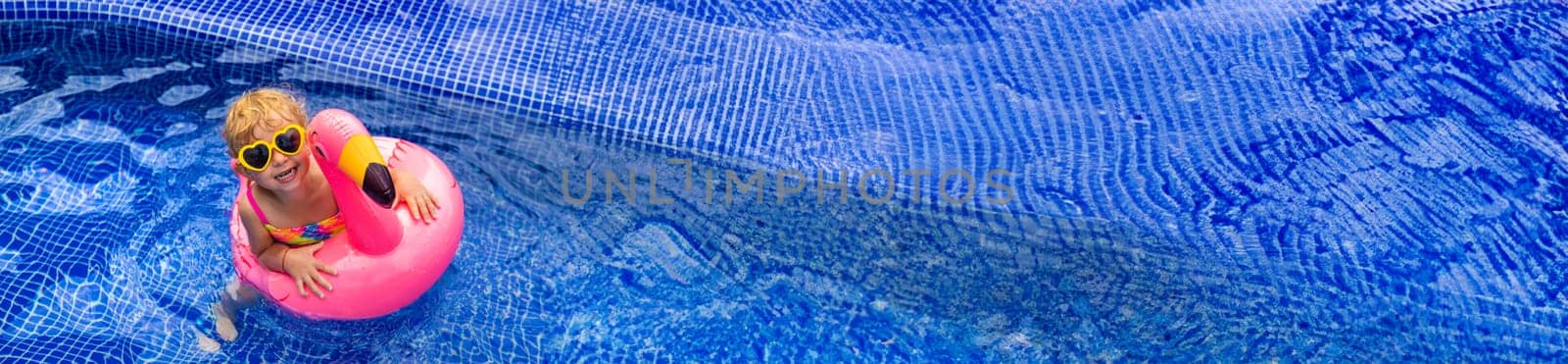 A child in a pool swims in a circle of flamingos. Selective focus. Kid.