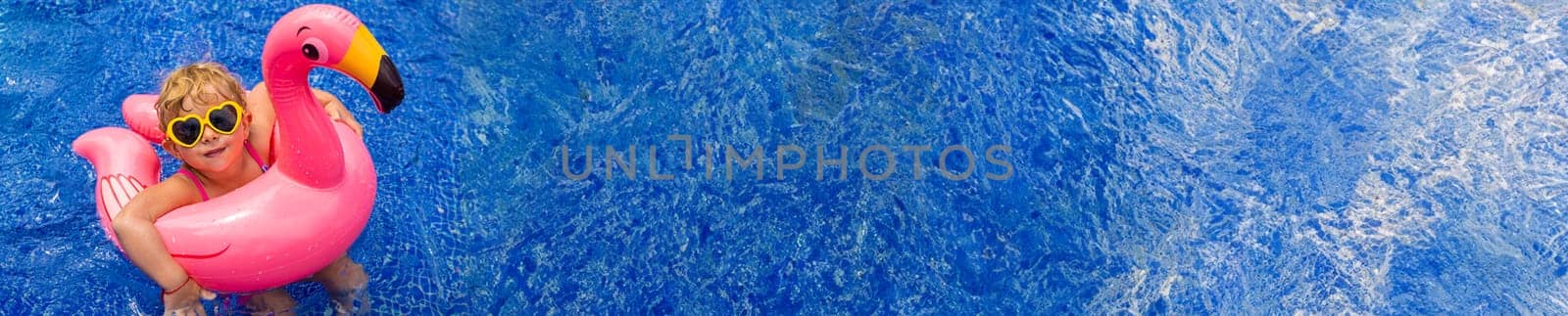 A child in a pool swims in a circle of flamingos. Selective focus. Kid.