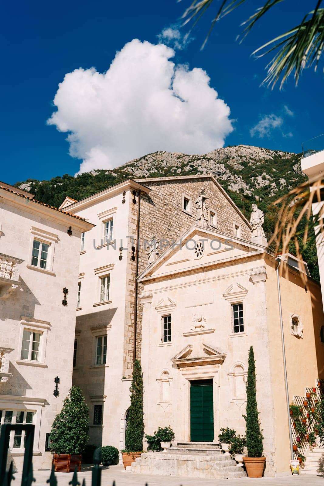 Church of St. Mark the Apostle among ancient houses and green trees in flowerpots. Perast, Montenegro. High quality photo