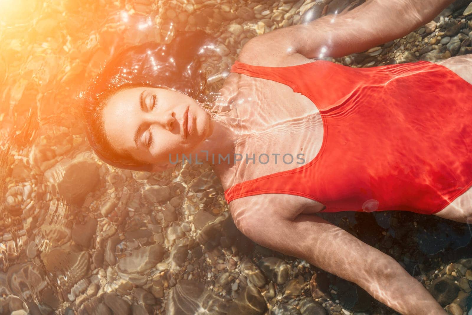 Woman travel portrait. Close-up portrait of a happy woman with long hair in a red bikini, floating in water and smiling at the camera. by panophotograph