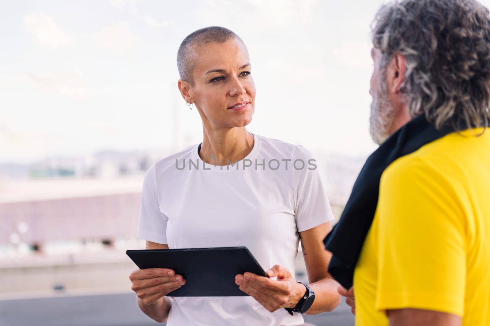 female personal trainer watching progress of workout on a tablet and discussing the results with senior sportsman, concept of healthy and active lifestyle