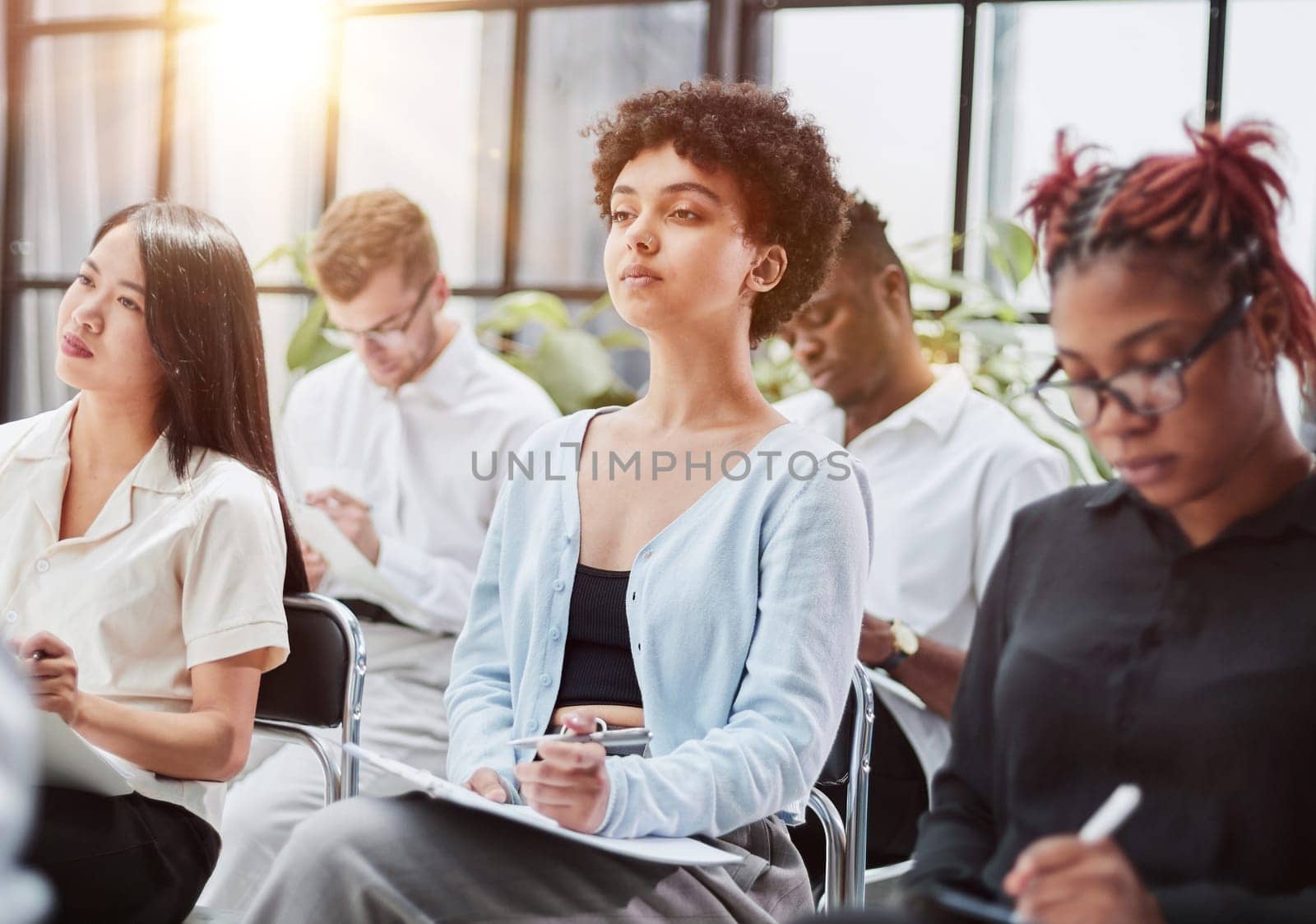 Interested happy young multiracial colleagues sitting on chairs, listening to male boss team leader by Prosto