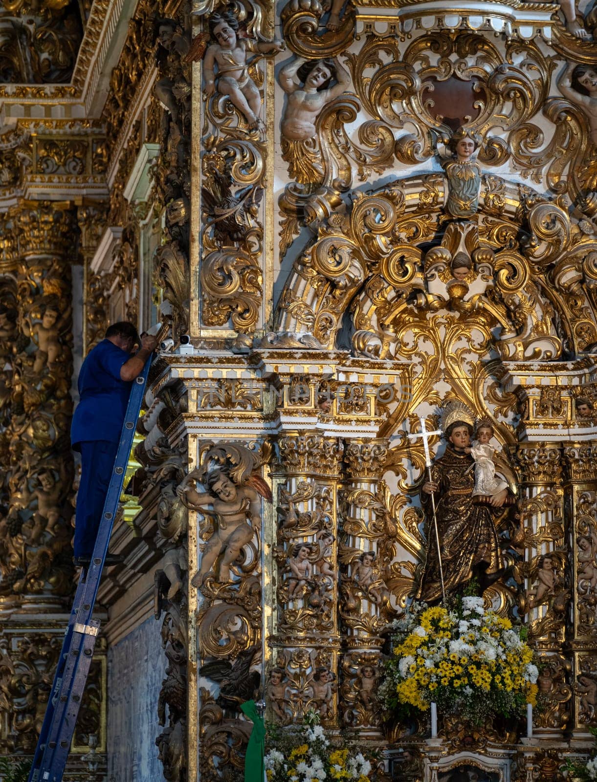 Worker on ladder blends with lavish church decor.