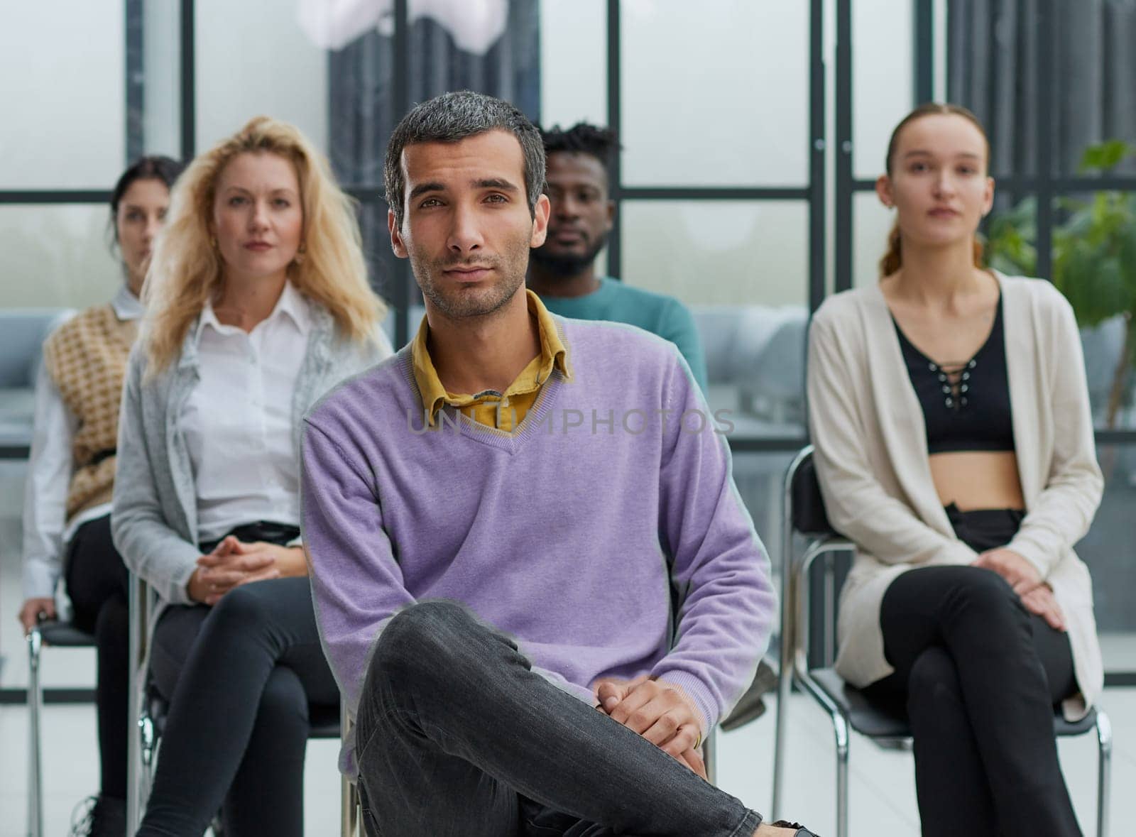 a young businessman in a purple sweater sits against the background of his colleagues in a modern office by Prosto