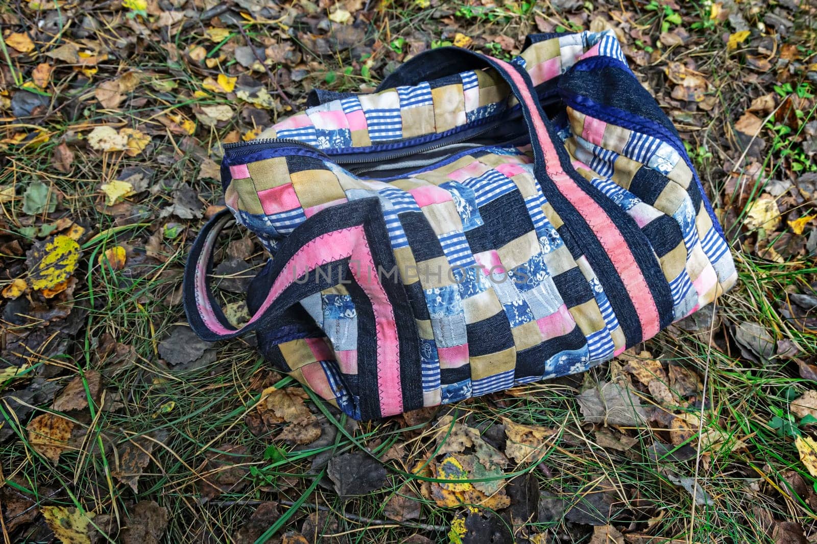 Beautiful women's picnic bag of colorful scraps of fabric in patchwork on the background of autumn leaves. Handmade.