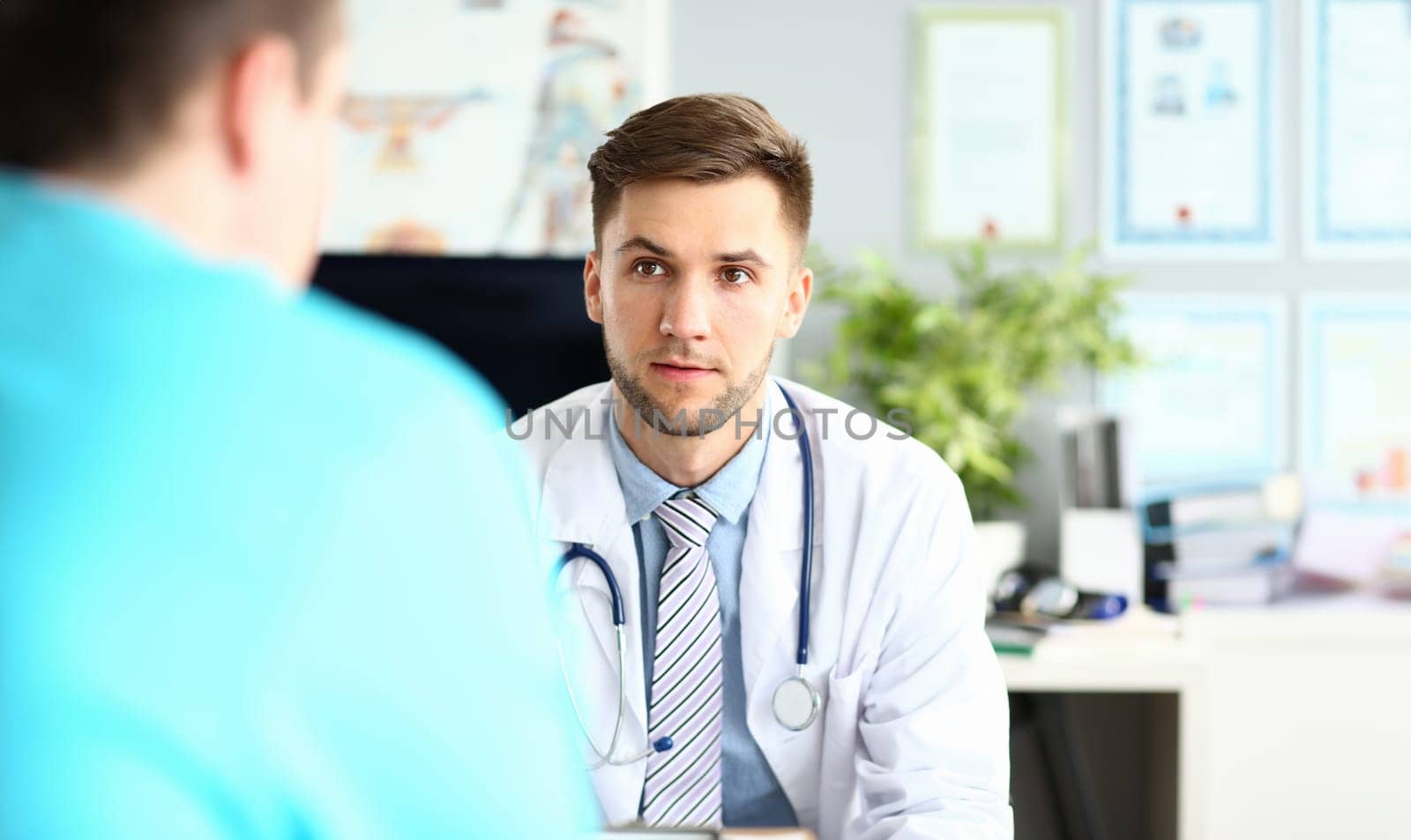 Portrait of worried physician talking and looking at colleague with fear and disturbance. Concerned man wearing stethoscope and white robe with striped tie. Medical treatment concept