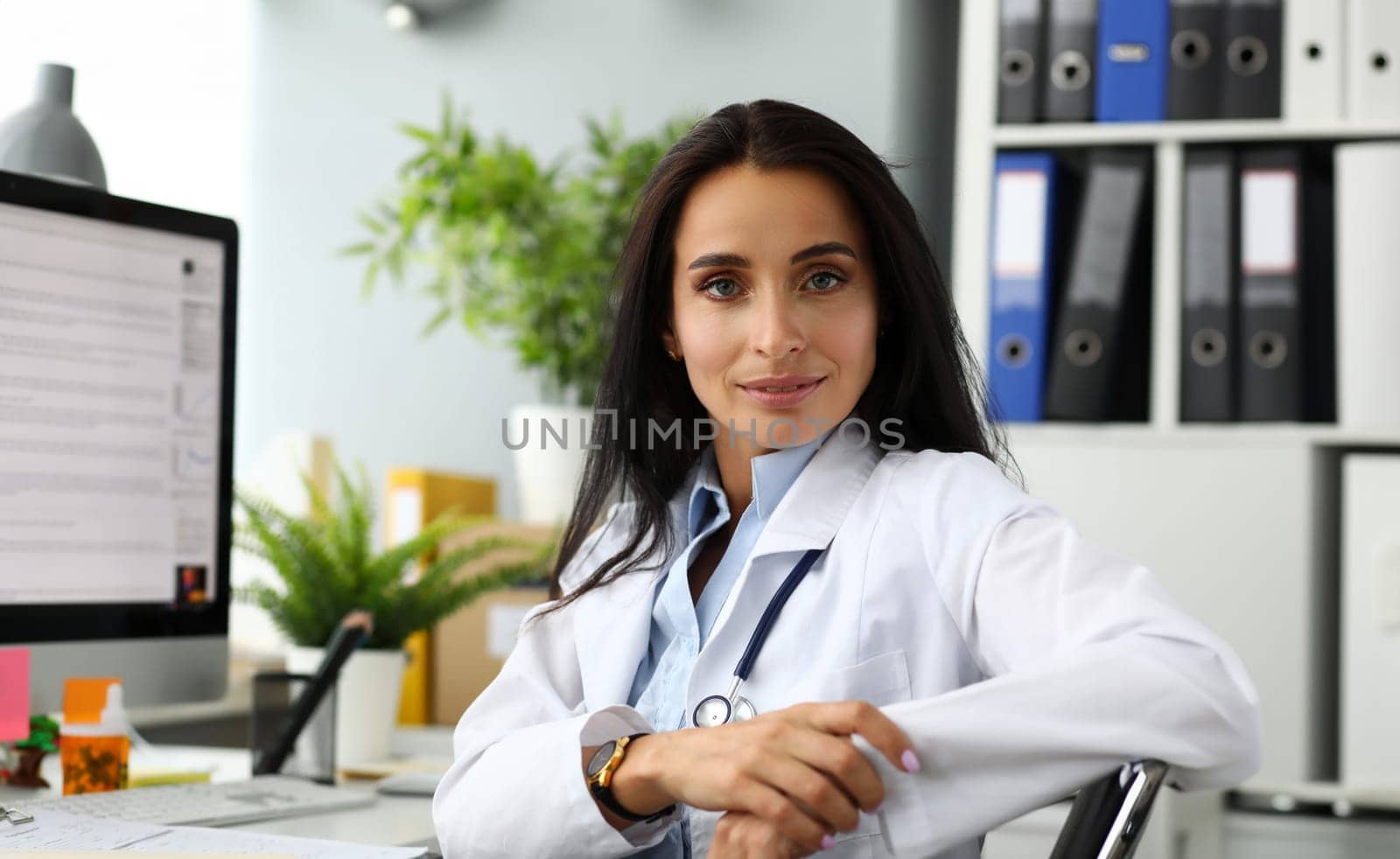 Mature female GP sitting at working table arms crossed looking in camera portrait