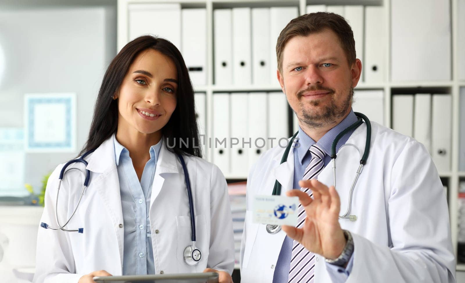 Group of smiling mature caucasian doctors offering special plastic card for medical services sale portrait