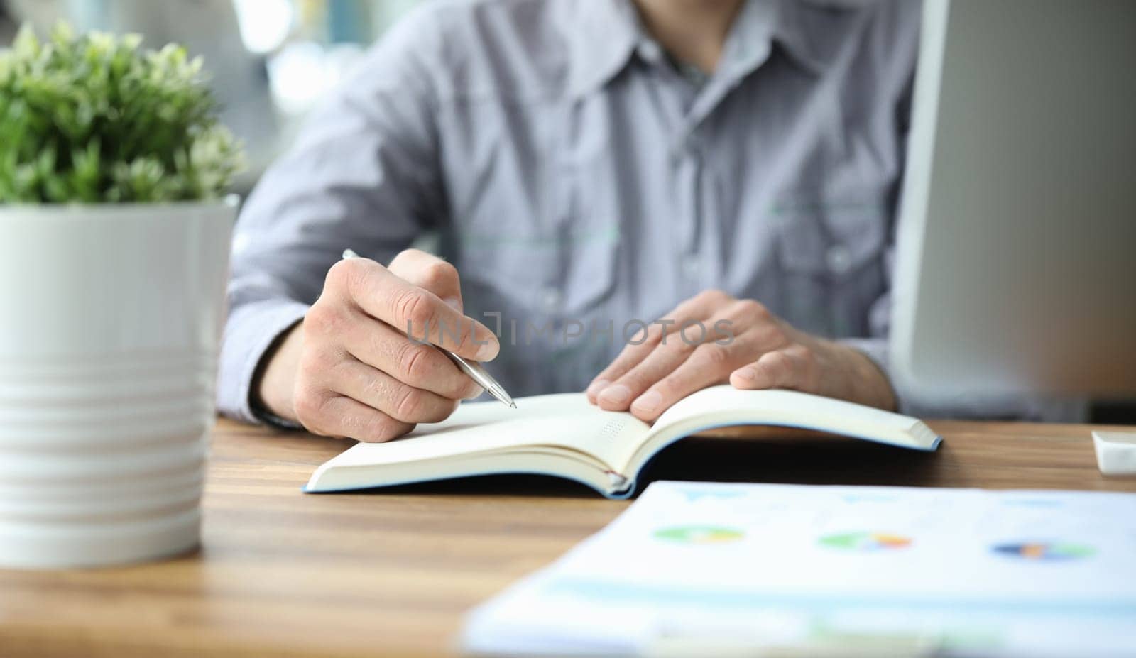 Businessman sits at a table holds pen in his hands and writes in notebook. Business education concept