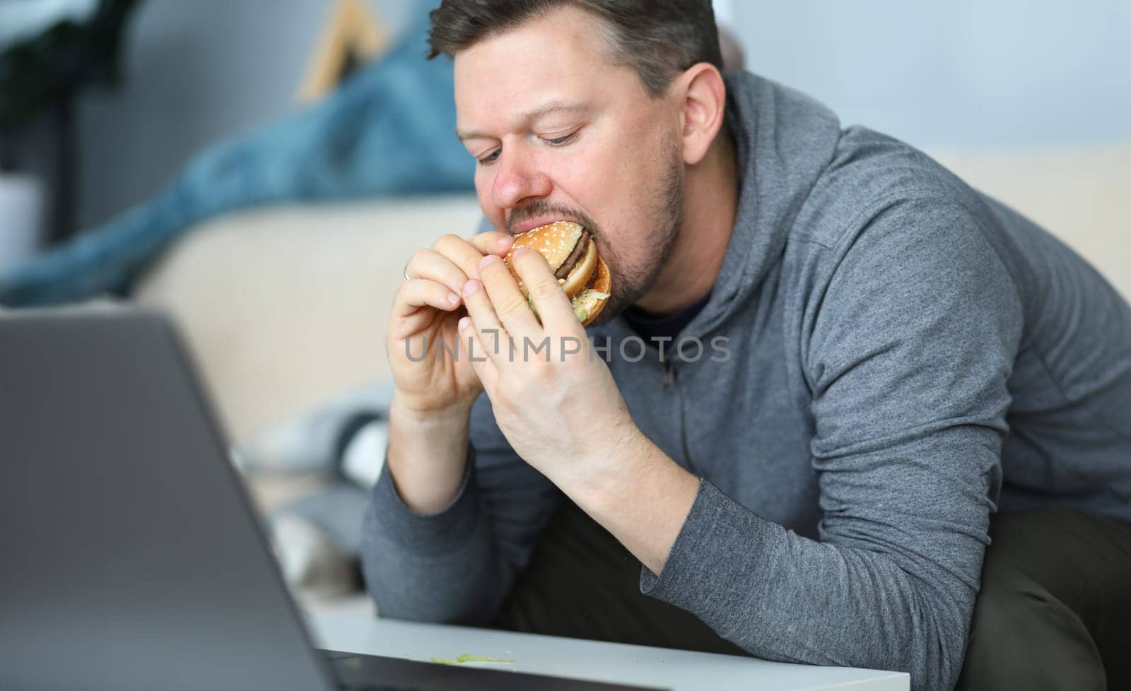 Man sit on sofa and eating burger against flat by kuprevich