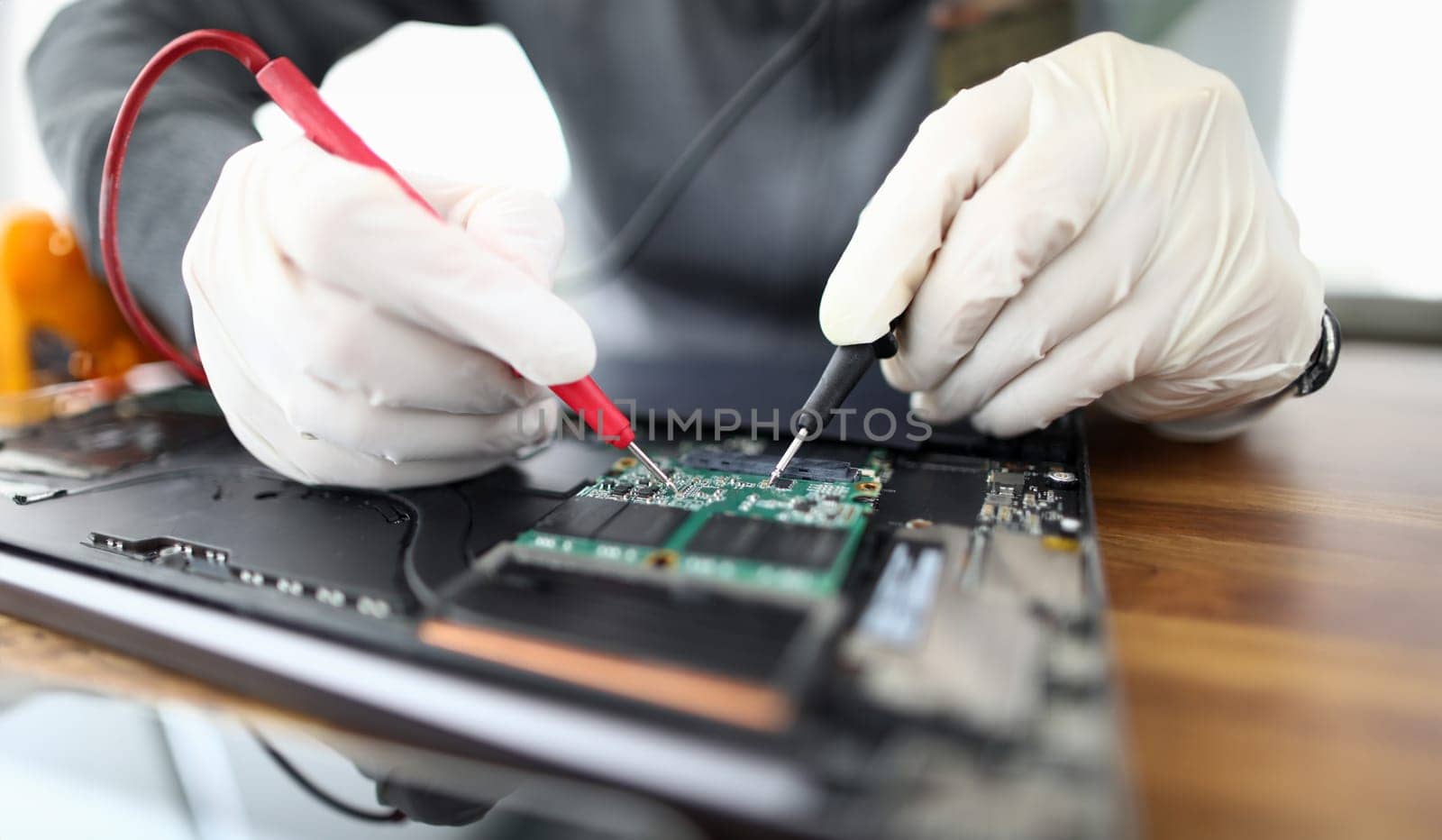 Male hands in white protective glove hold contact probe an electronic circuit tester. Laptop repair and technology concept