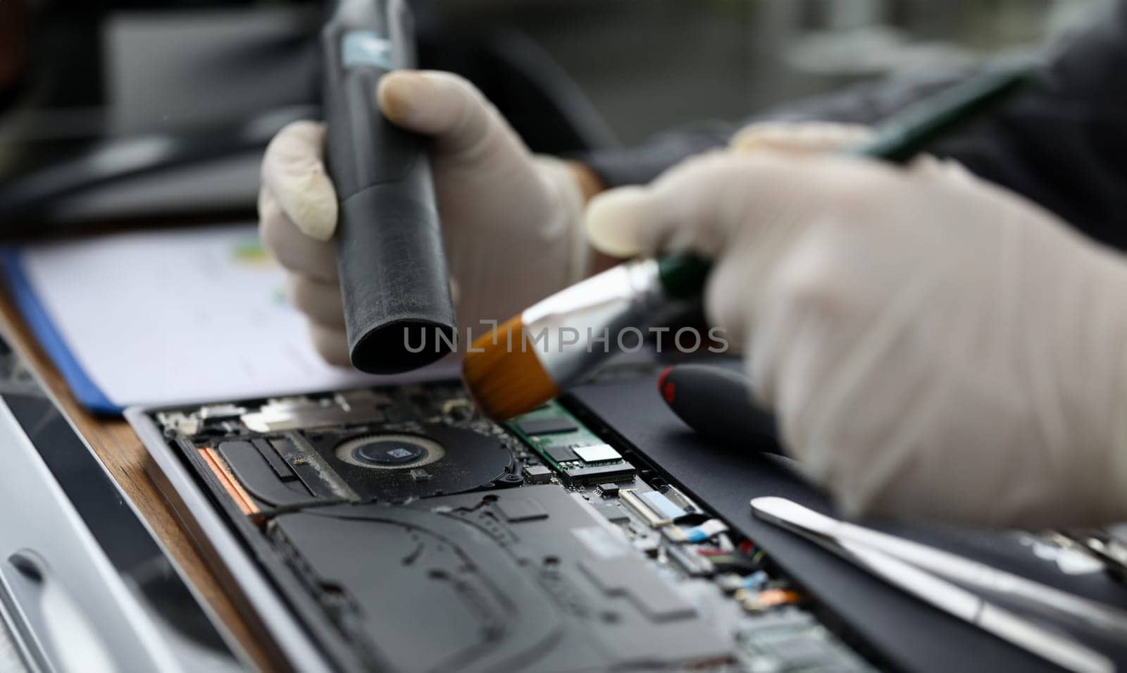 Male chemist in white protective gloves use vacuum cleaner in laptop repair service. Technical prevention of device performance and protection against overheating concept