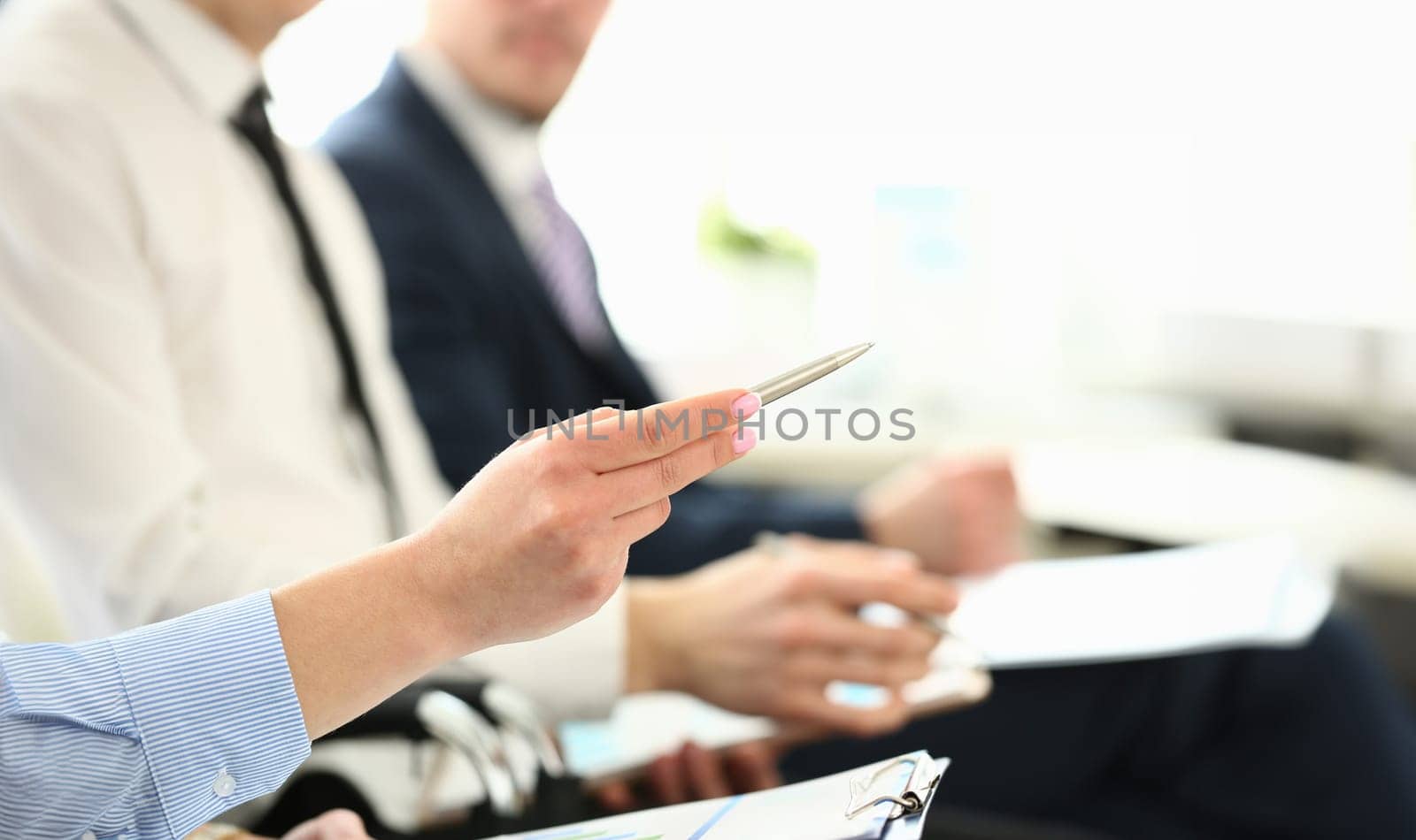 Focus on attractive female with great manicure pointing at something in big modern office. Friendly colleagues discussing new business project. Company meeting concept. Blurred background
