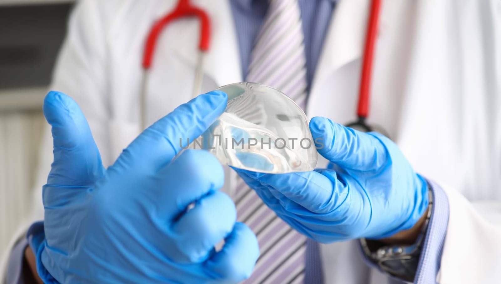 Male doctor hand in blue protective gloves hold new fashion silicone breast implant closeup. Plastic corrective surgery excel concept