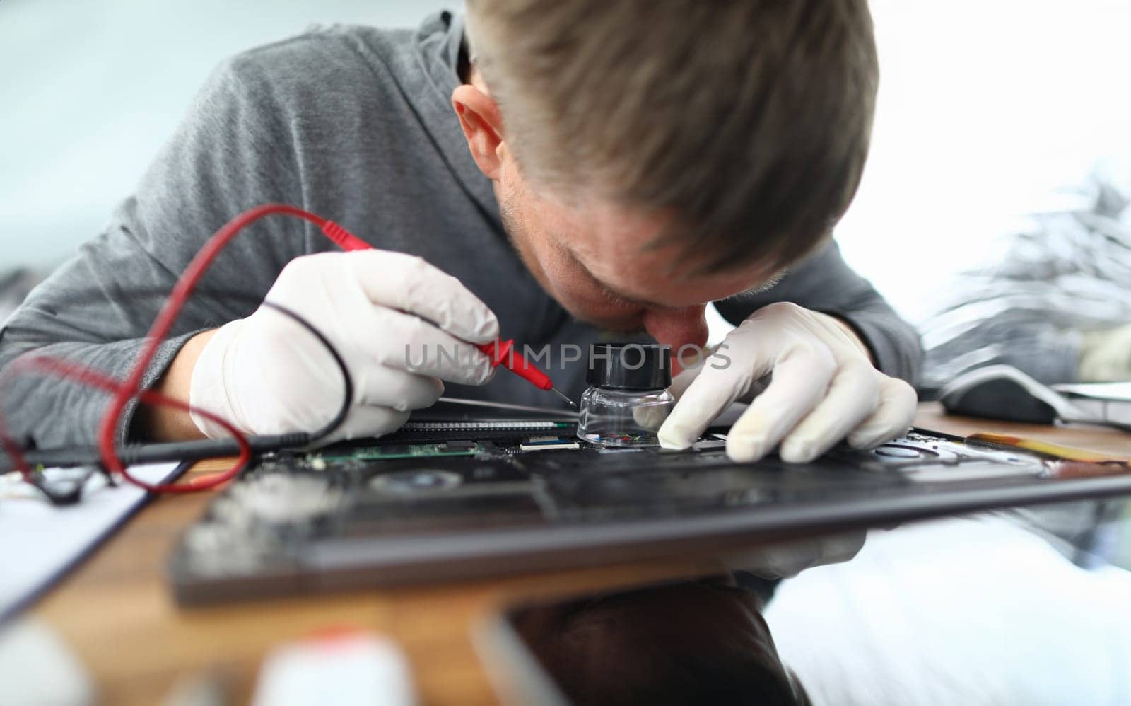 Male hands in white protective gloves with lens hold contact probe an electronic circuit tester. Laptop repair and technology concept
