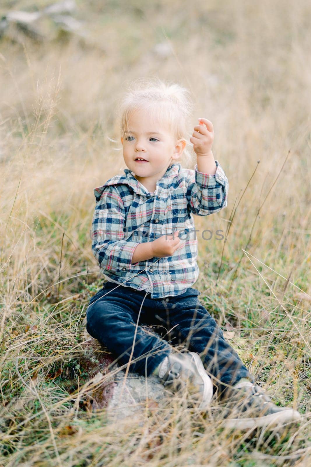 Little girl sits on a stone on the lawn and looks away with her hand up. High quality photo