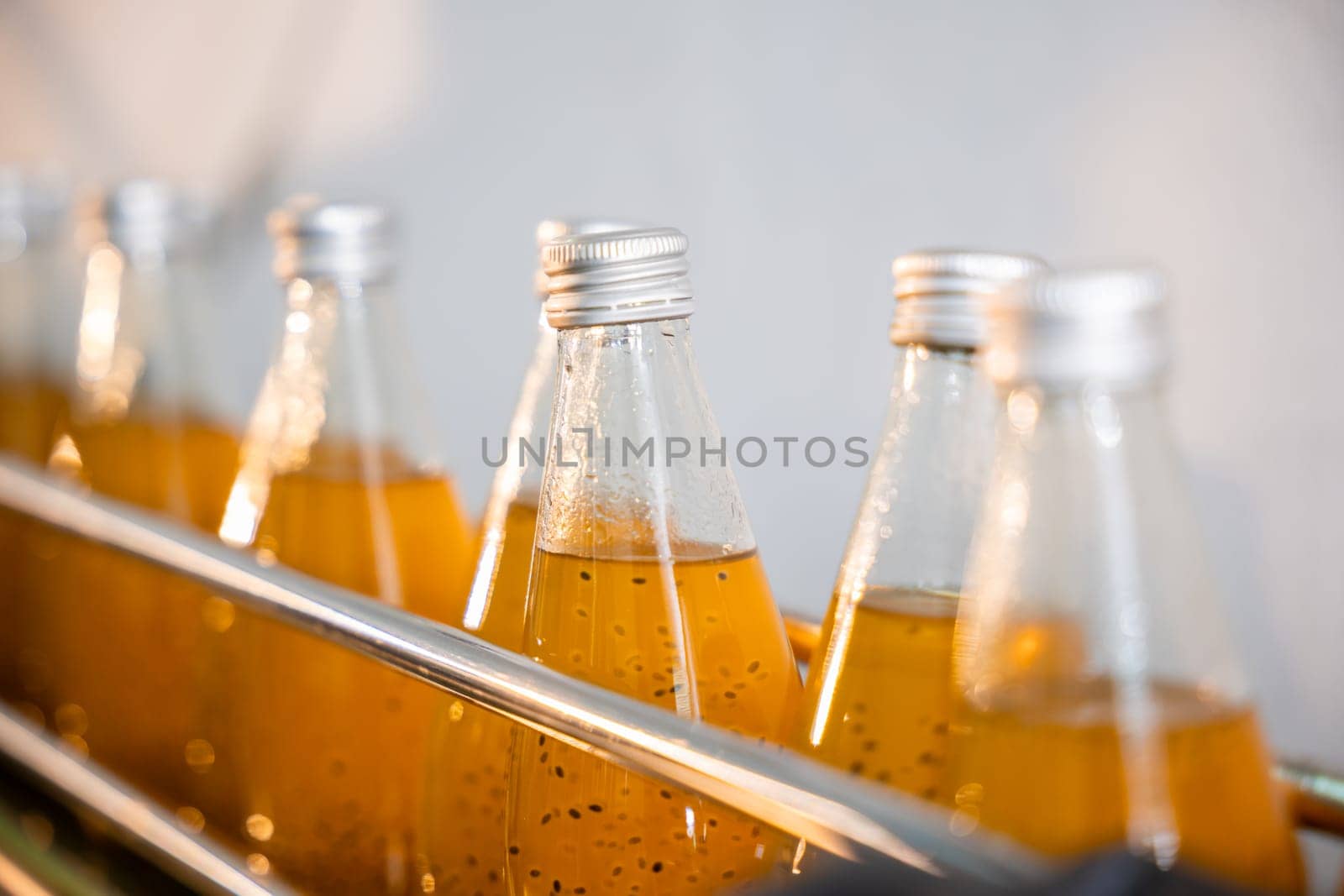 Transparent bottles move on a conveyor belt in a beverage factory filled with basil or chia seed drinks infused with pomegranate. Clean automated manufacturing is evident.
