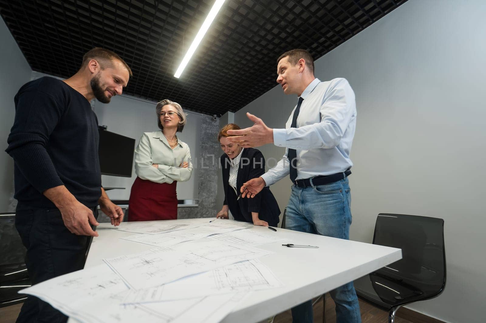 Four business people review and discuss blueprints. Designers engineers at a meeting