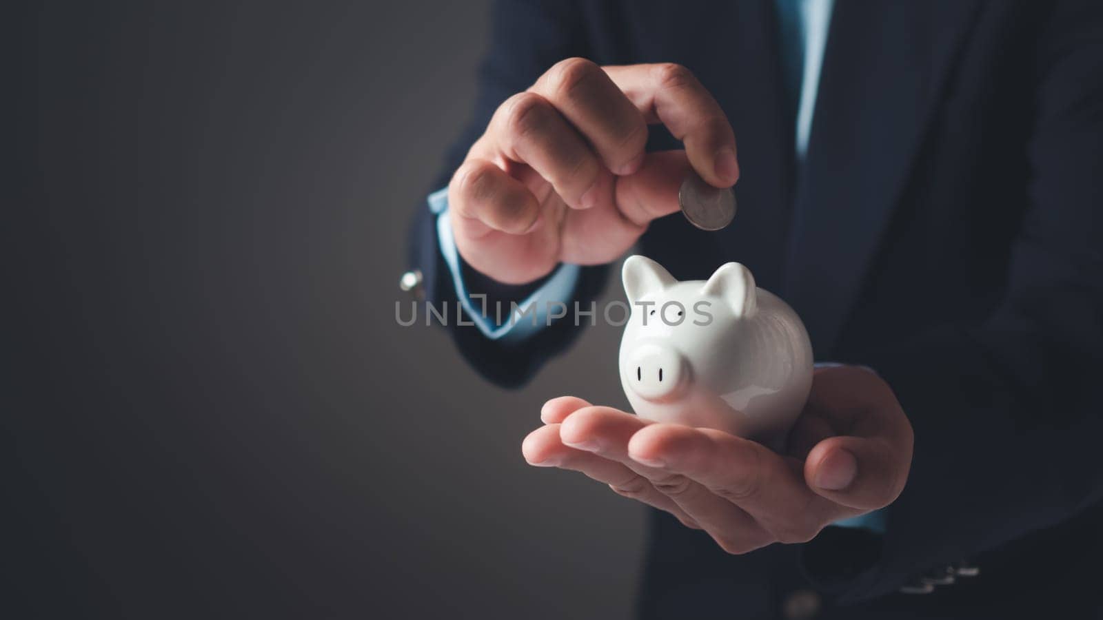 Businessman in suit is holding piggy bank. Finance Savings concept, Money saving and deposit for investment to get profit and dividend concept, Planning to income for savings and paying off expenses. by Unimages2527