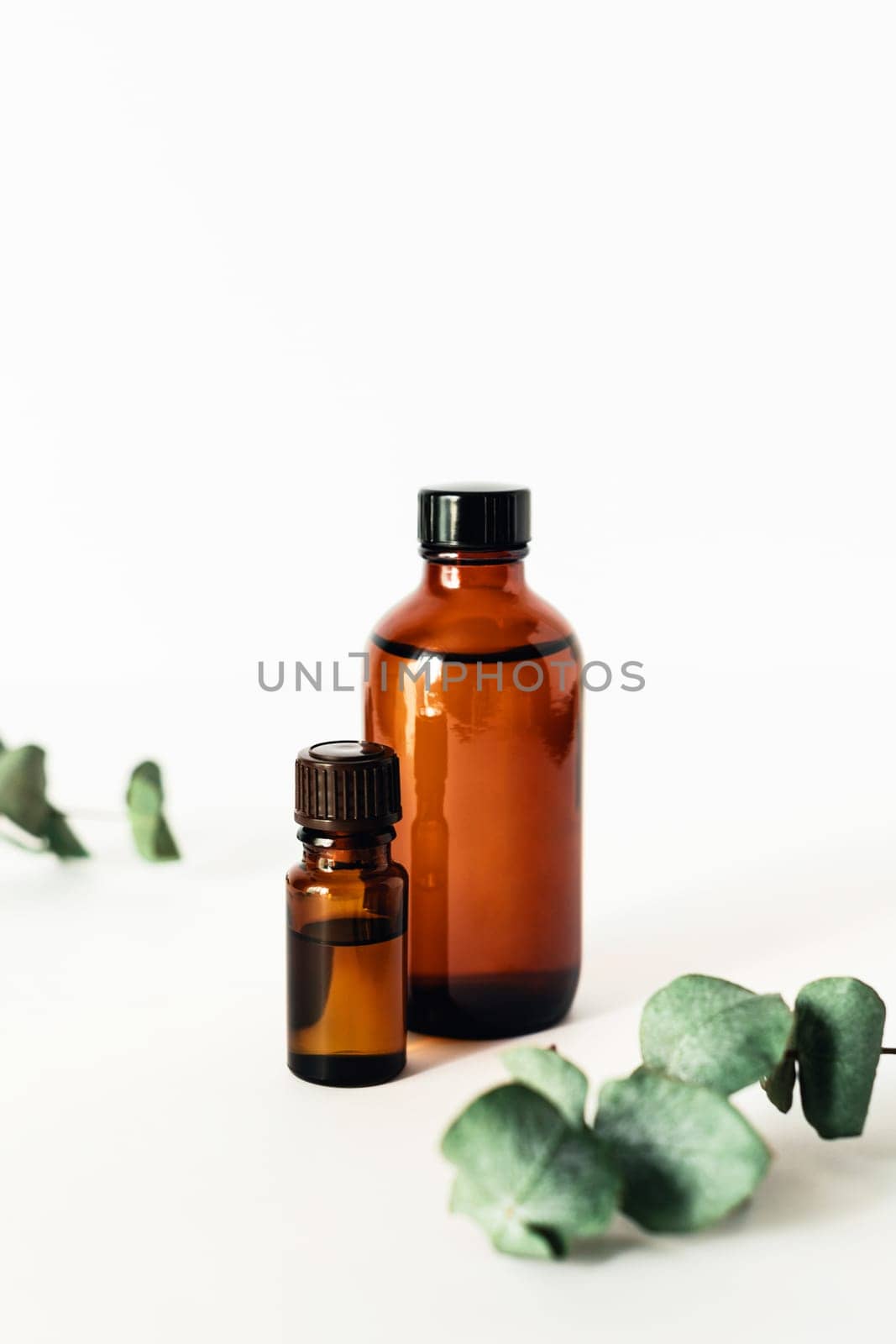 Two bottles of fragrant cosmetic or essential oil on a white background surrounded by sprigs of eucalyptus. Stay home and be mentally healthy.