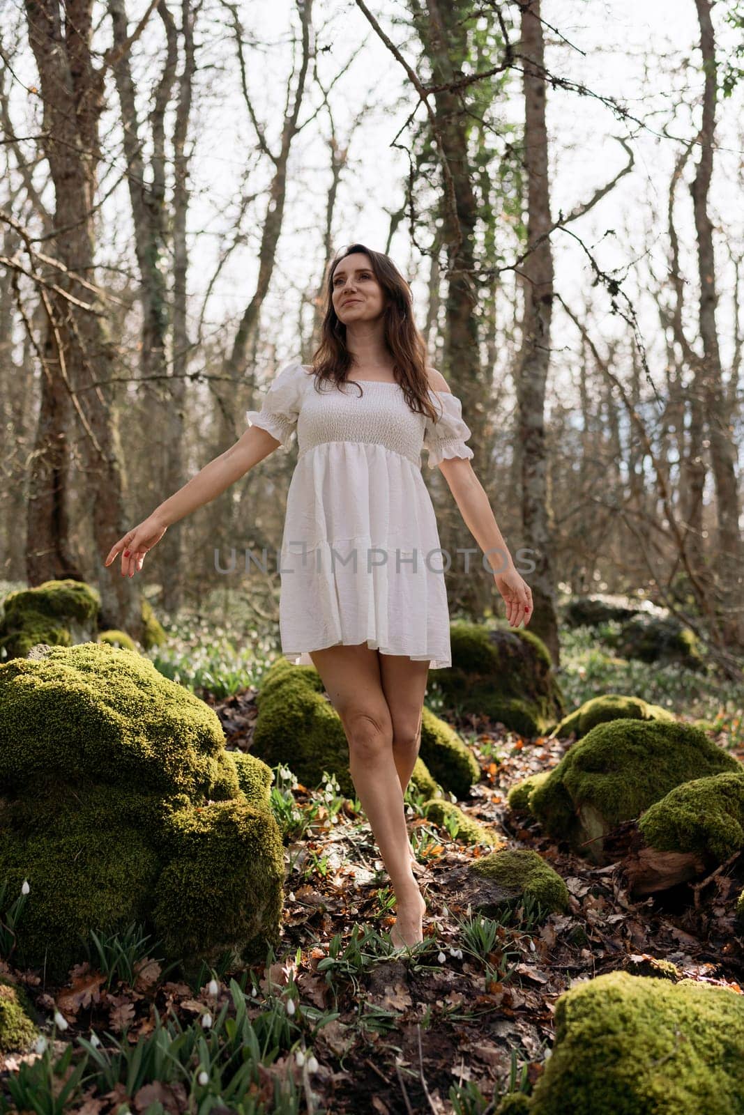 Snowdrops galanthus woman. She stands in a white dress on a meadow with snowdrops in a spring forest by Matiunina