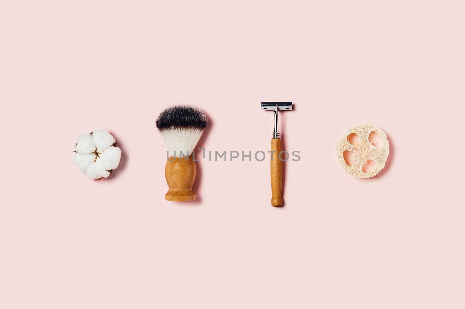 Natural bamboo sponge, shaver brush, razor and cotton flower on pink background. Flat lay, top view.