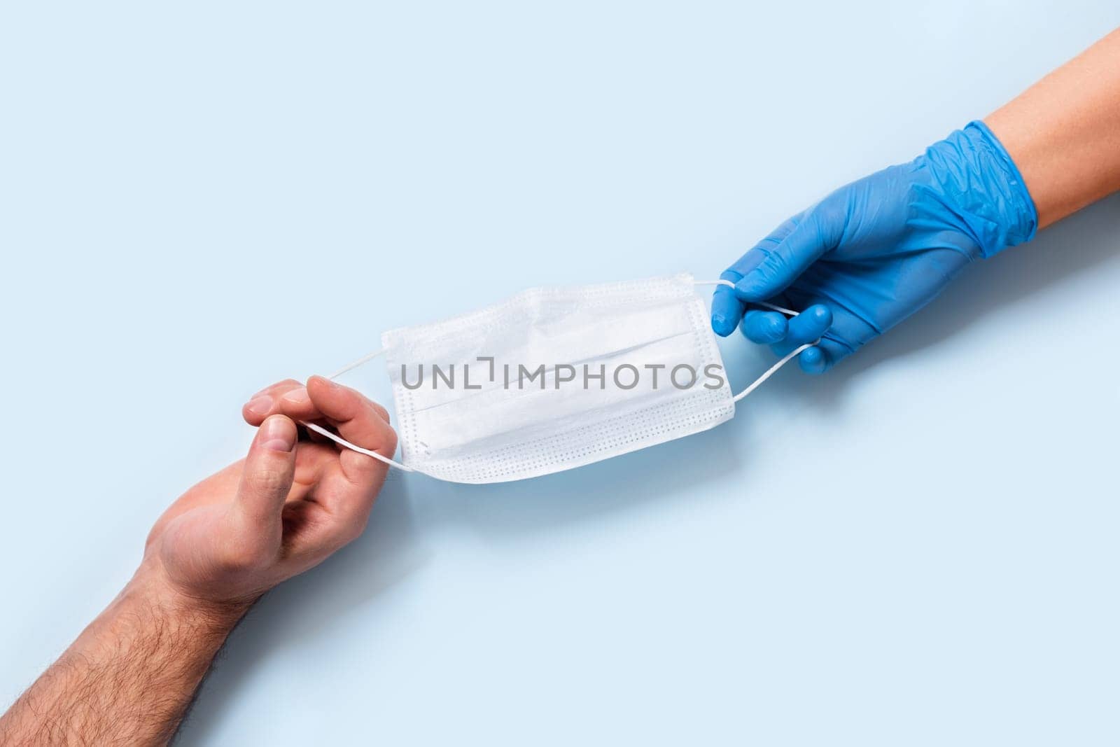 Men's and women's hands in latex gloves holding one medical mask.