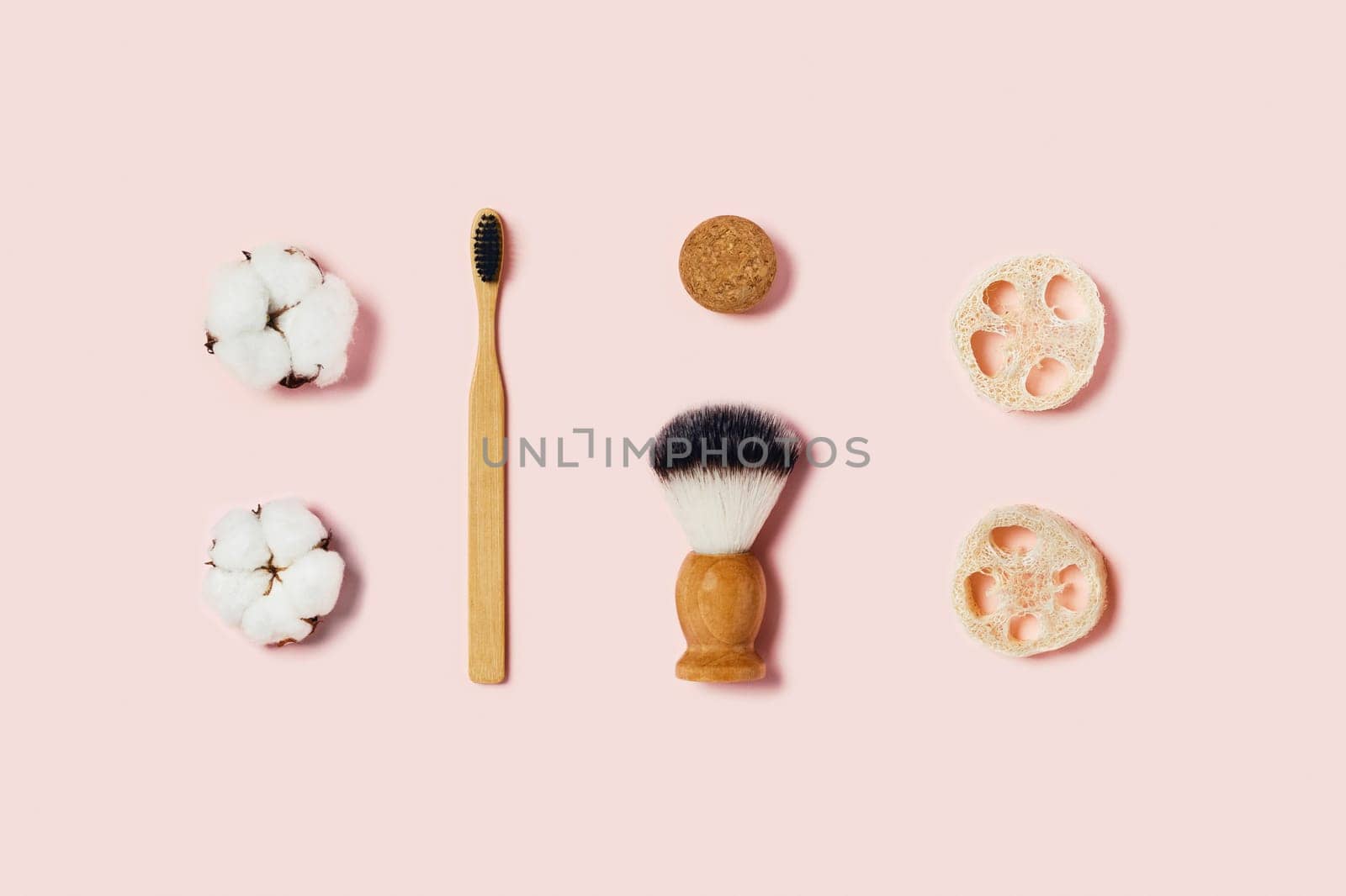 Bathroom accessories on pink background. Natural bamboo toothbrush, sponges, cotton flowers, shaving brush. Flat lay, top view.