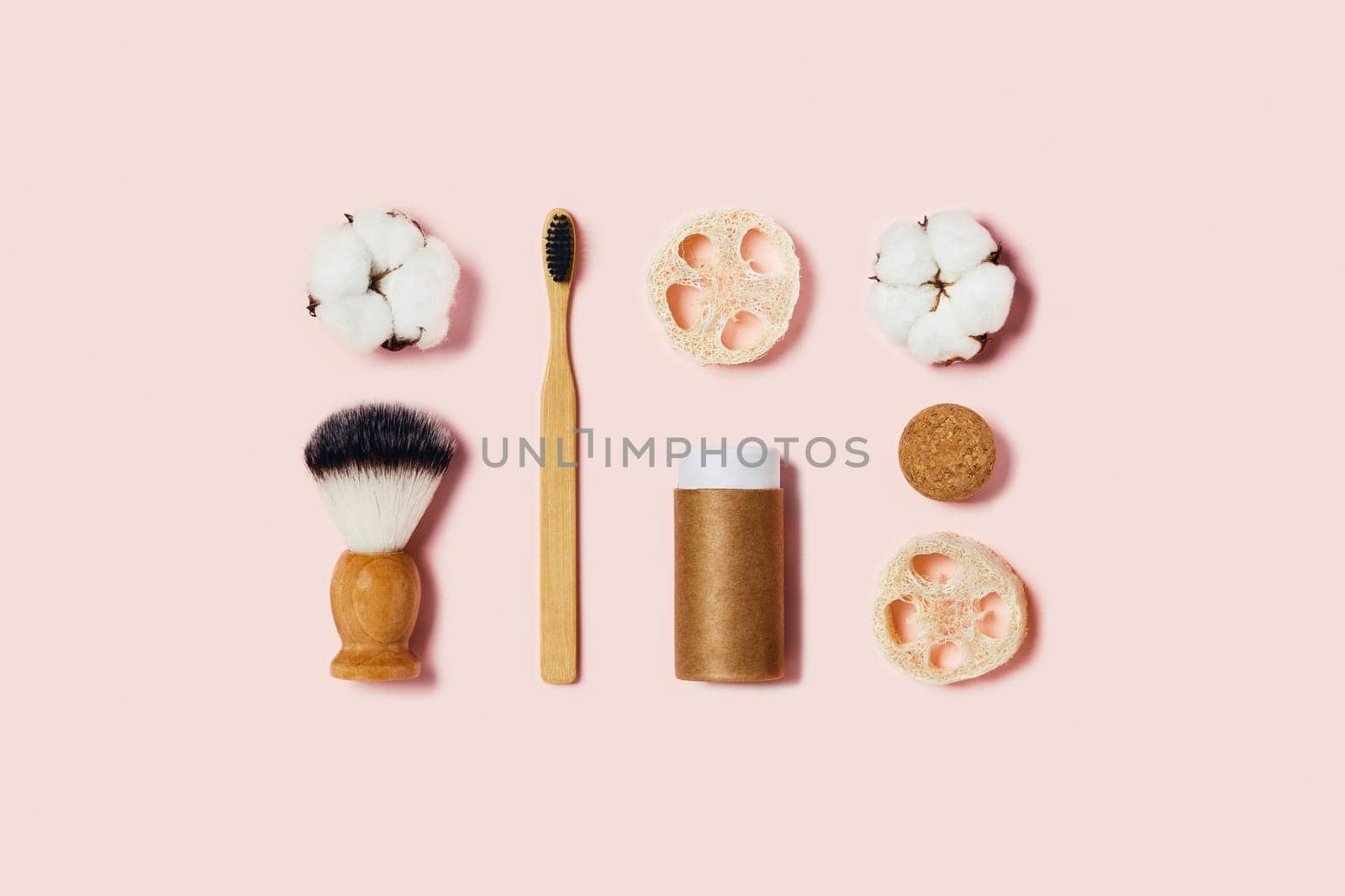 Natural bamboo toothbrush, paper tube, natural sponges, cotton flowers on pink background. Flat lay, top view.