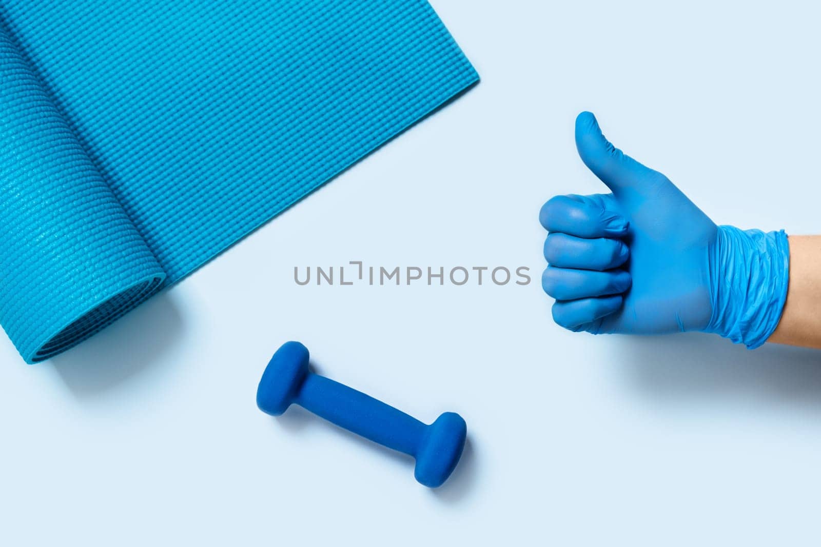 Train at home - protect yourself and others from disease. A woman's hand in medical gander holds a dumbbell.