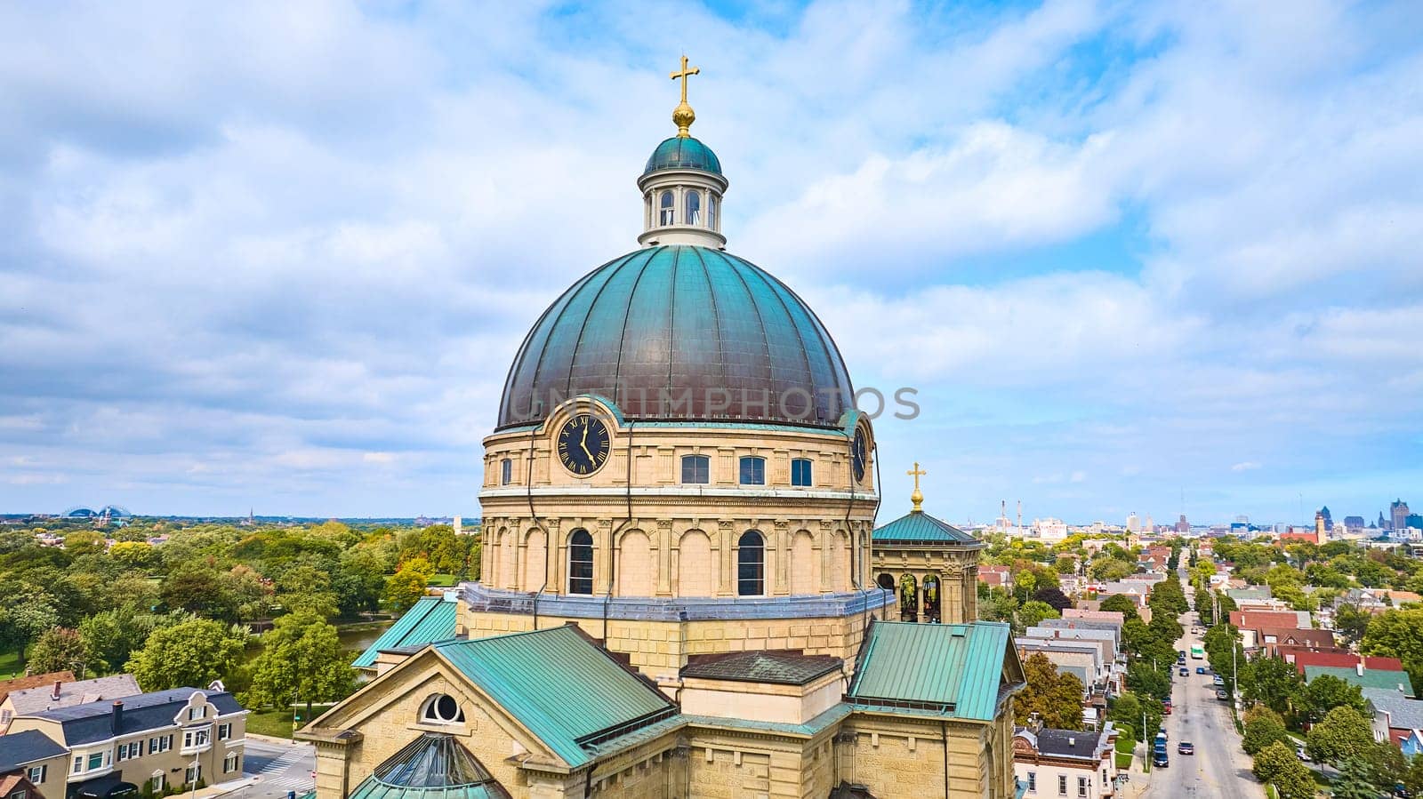 Aerial view of the Basilica of St Josaphat with golden cross and green dome in Milwaukee, Wisconsin, set against a vibrant cityscape under clear skies.