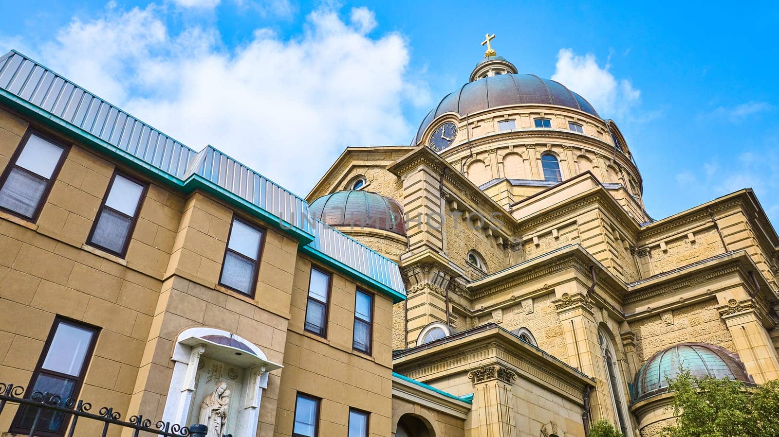 Aerial view of Basilica of St Josaphat in Milwaukee, Wisconsin, showcasing its grand dome, cross, and classical architecture against a modern cityscape under a clear blue sky.