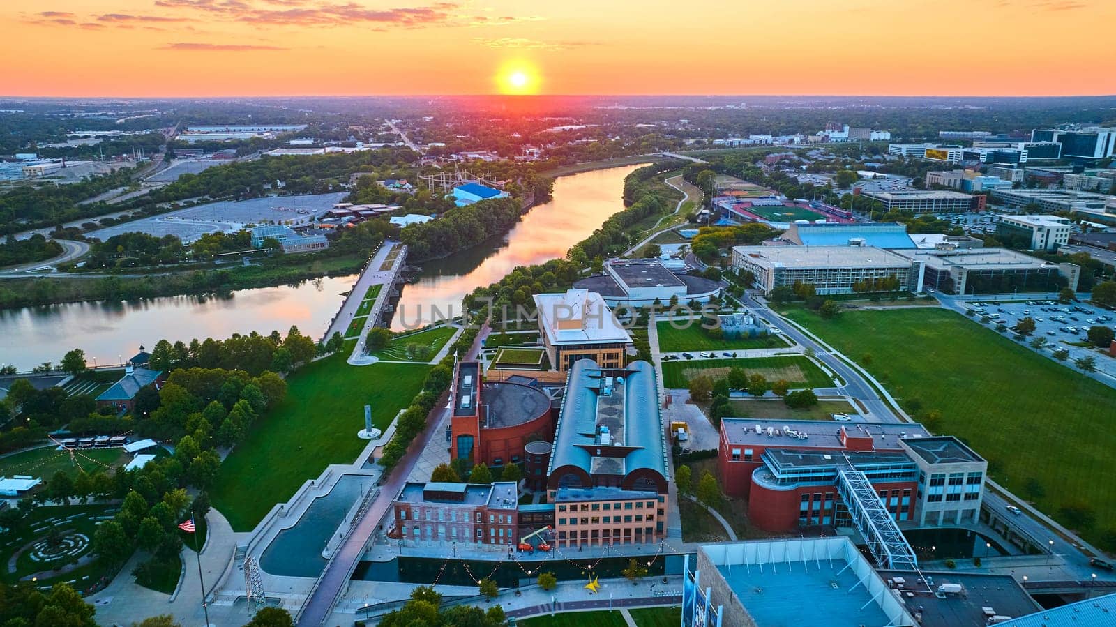 Aerial View of Indianapolis at Golden Hour - A drone captures the stunning sunset over the cityscape, highlighting the blend of modern and traditional architecture along a tranquil river.