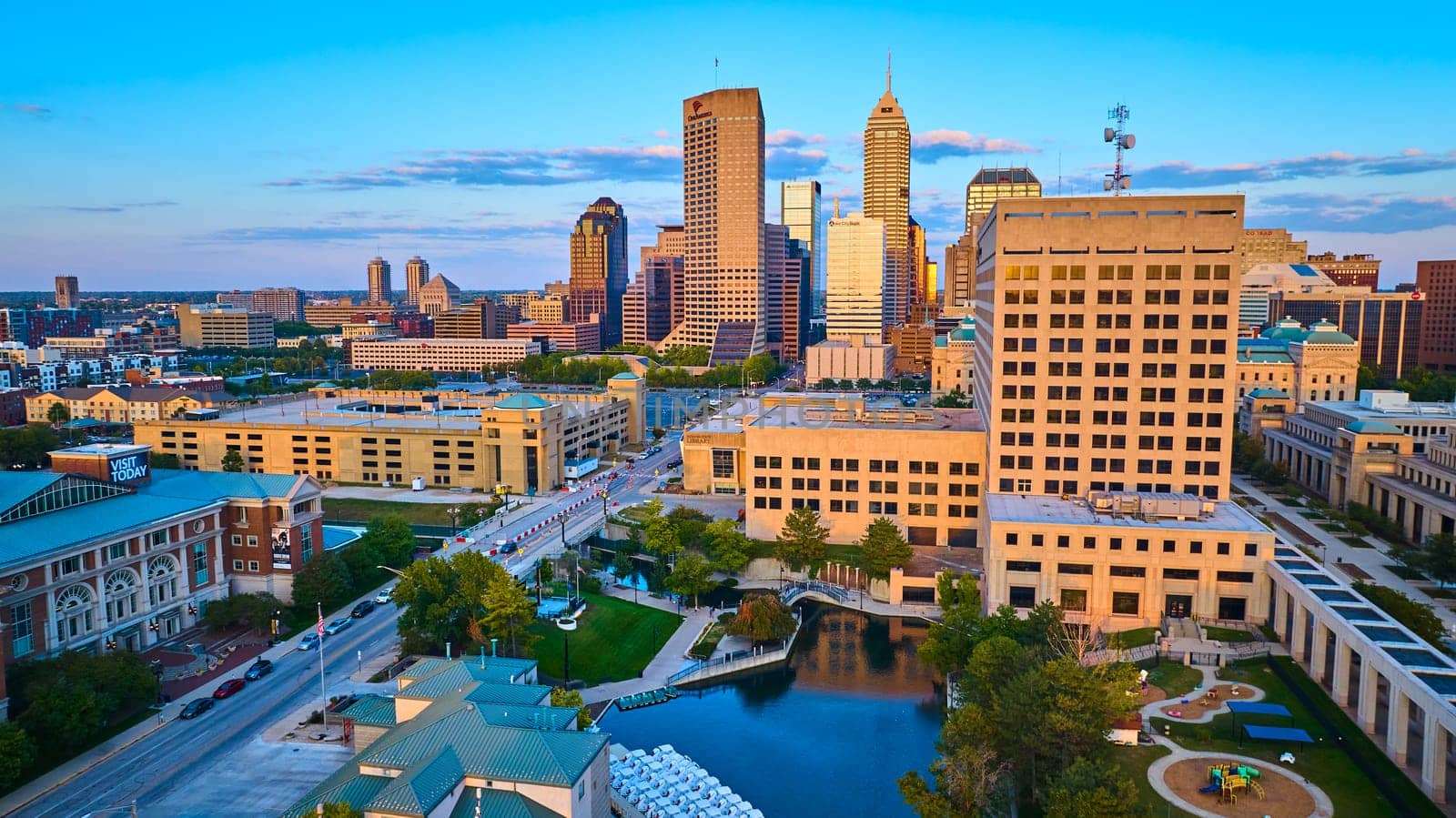 Aerial view of Indianapolis cityscape bathed in golden hour glow, highlighting urban planning with river intersection and recreational spaces.