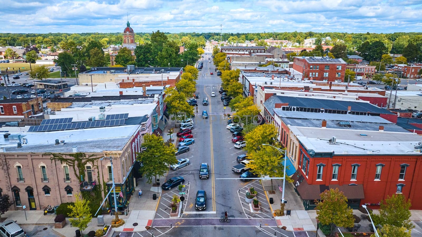 Aerial view of historic downtown Goshen, Indiana, showcasing a bustling main street lined with red brick buildings, the distinctive Elkhart County Courthouse, and the charm of small-town America during autumn.