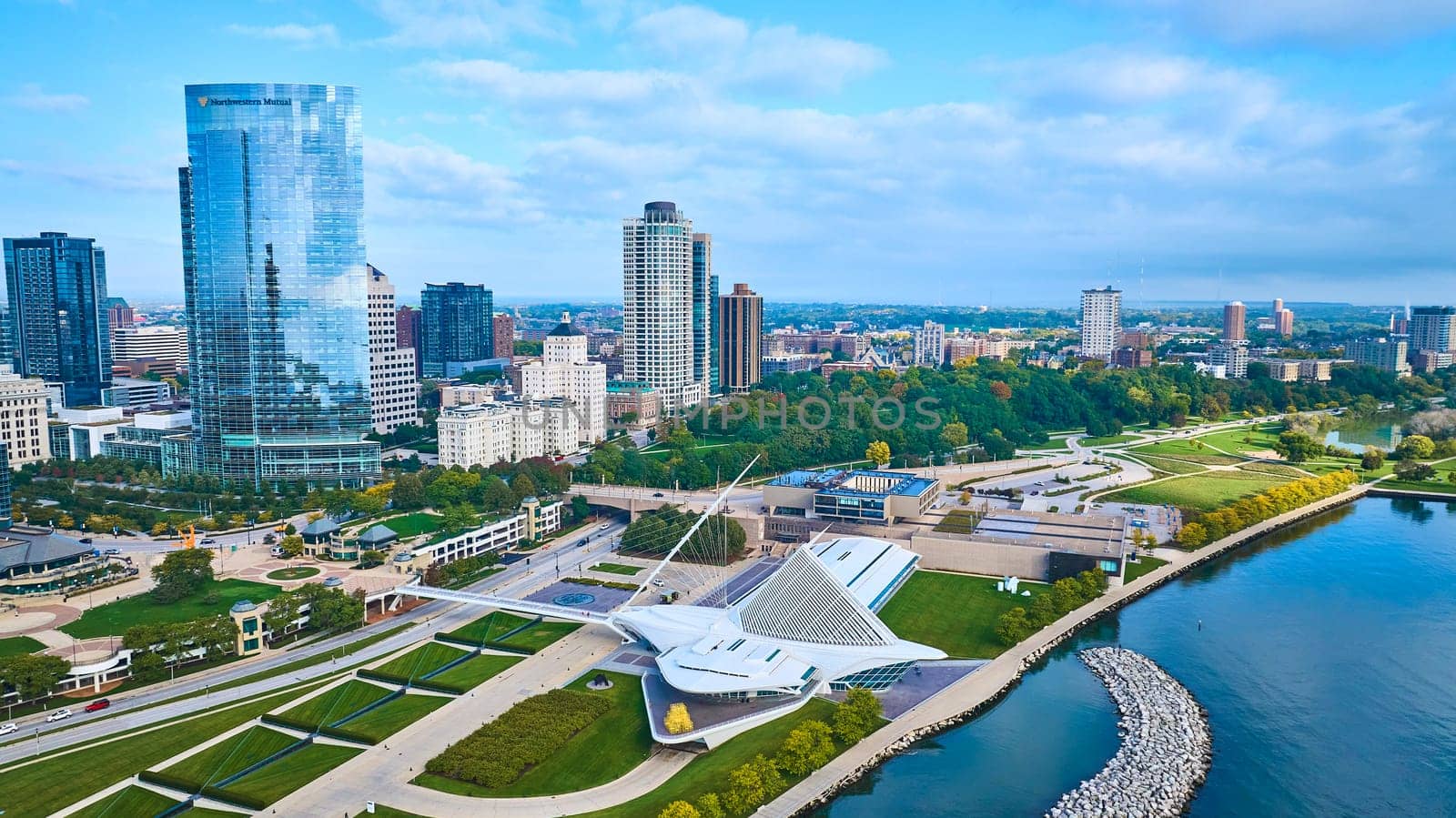 Vibrant aerial view of a modern cityscape featuring a glass skyscraper, the artistic Quadracci Pavilion in Milwaukee, and Lake Michigan, showcasing urban growth and sustainability