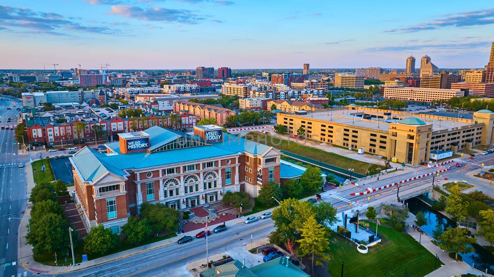 Sunset over Indianapolis in 2023, featuring the 'We Do History' cultural institution, residential and commercial buildings, and a bustling cityscape, captured via drone.