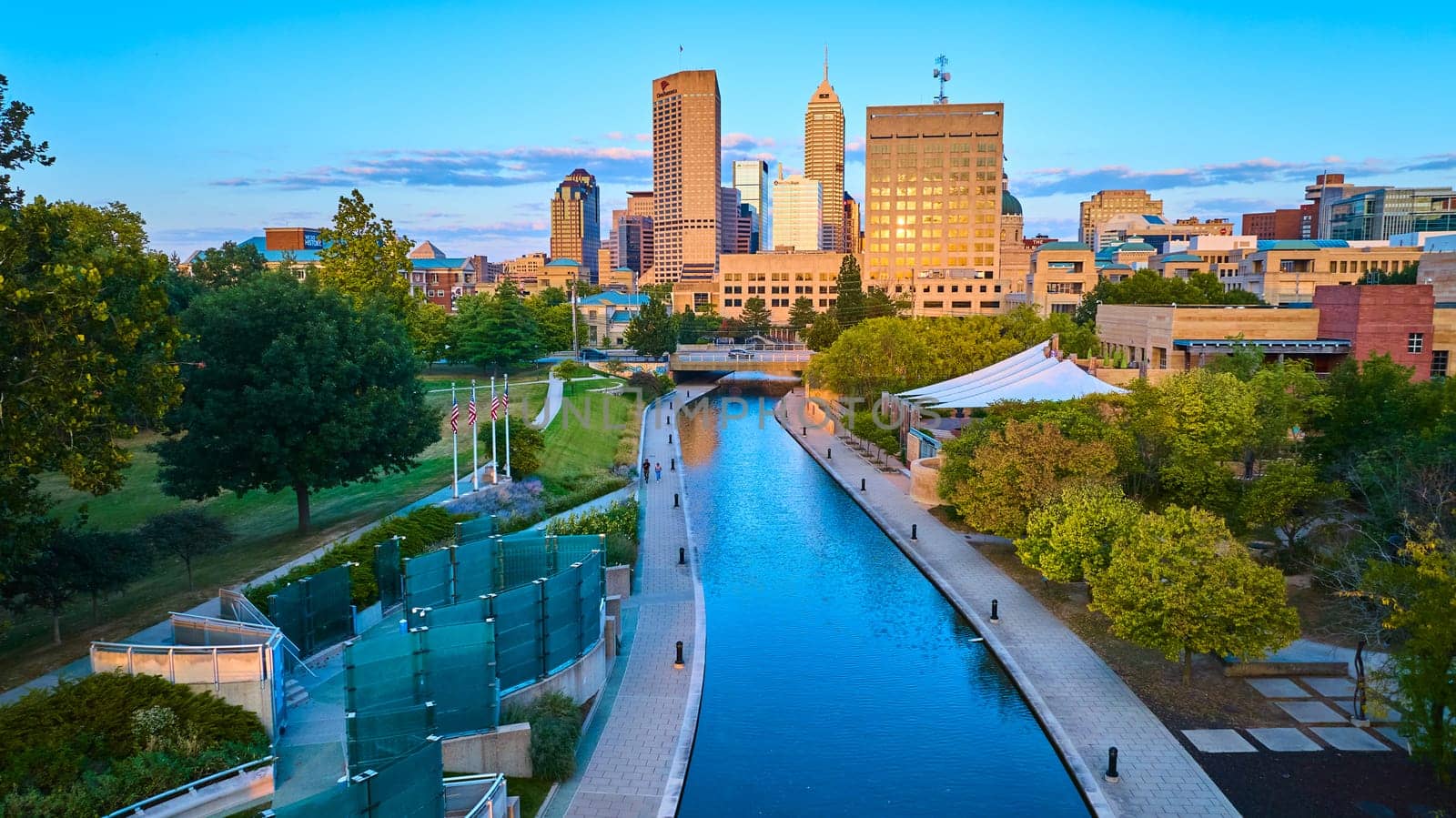 Golden hour over Indianapolis, showcasing serene river views, diverse architecture, and vibrant urban green spaces from an aerial perspective.