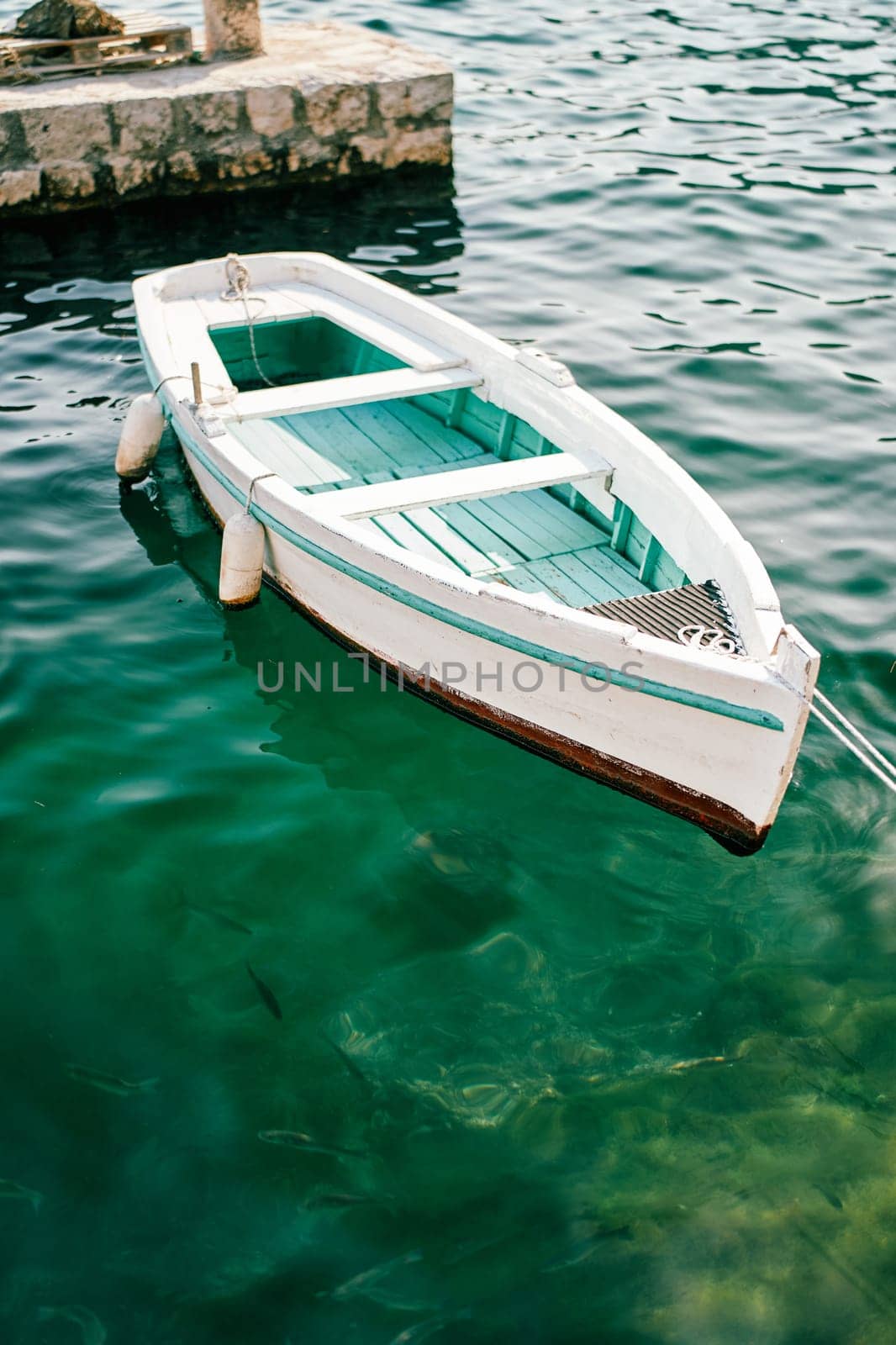 White fishing boat with a green bottom is moored at a stone pier. High quality photo