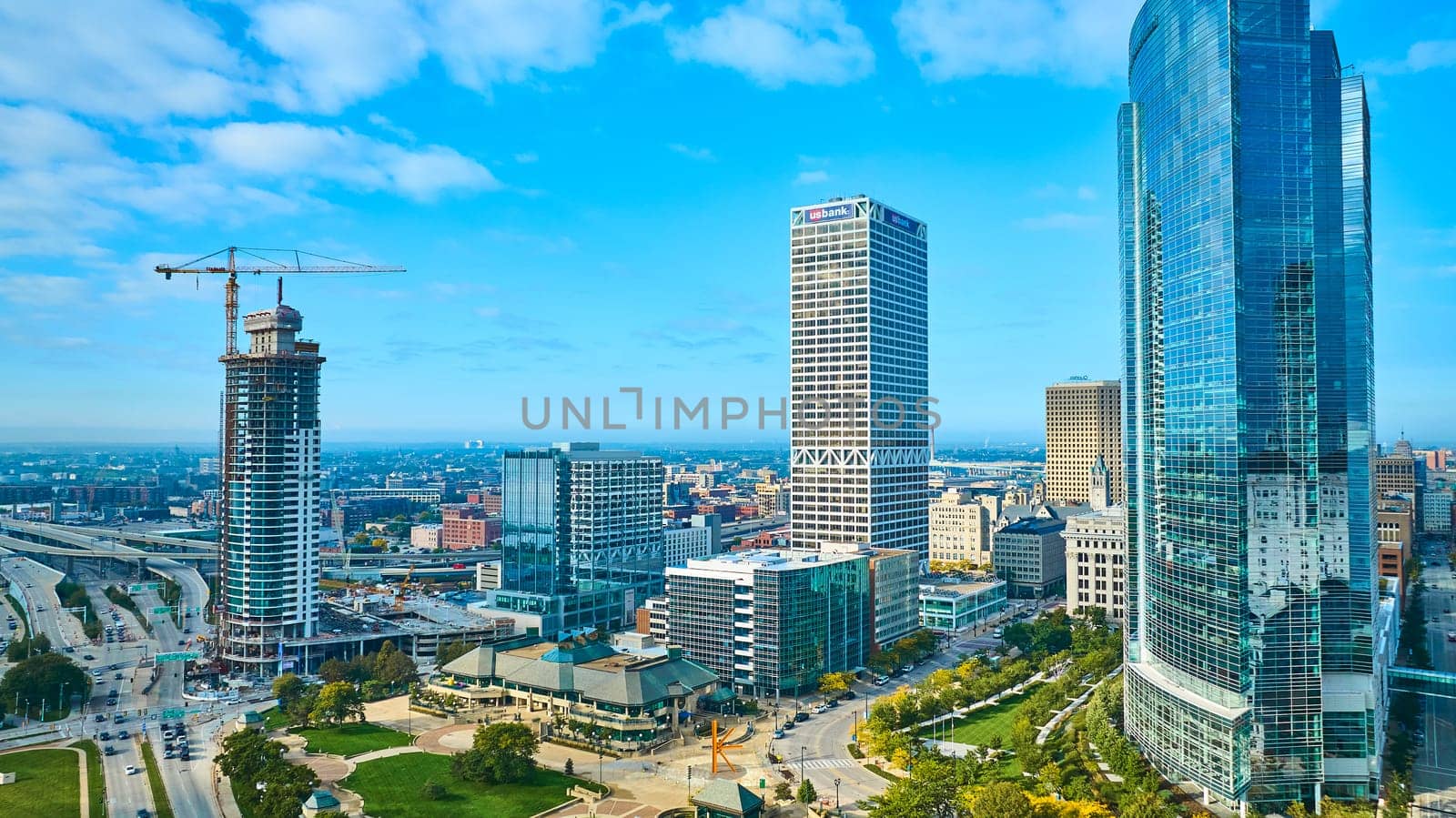 Bustling Milwaukee cityscape with towering skyscrapers, highlighted by sunlit glass facade and ongoing high-rise construction, reflecting urban growth and modernity.