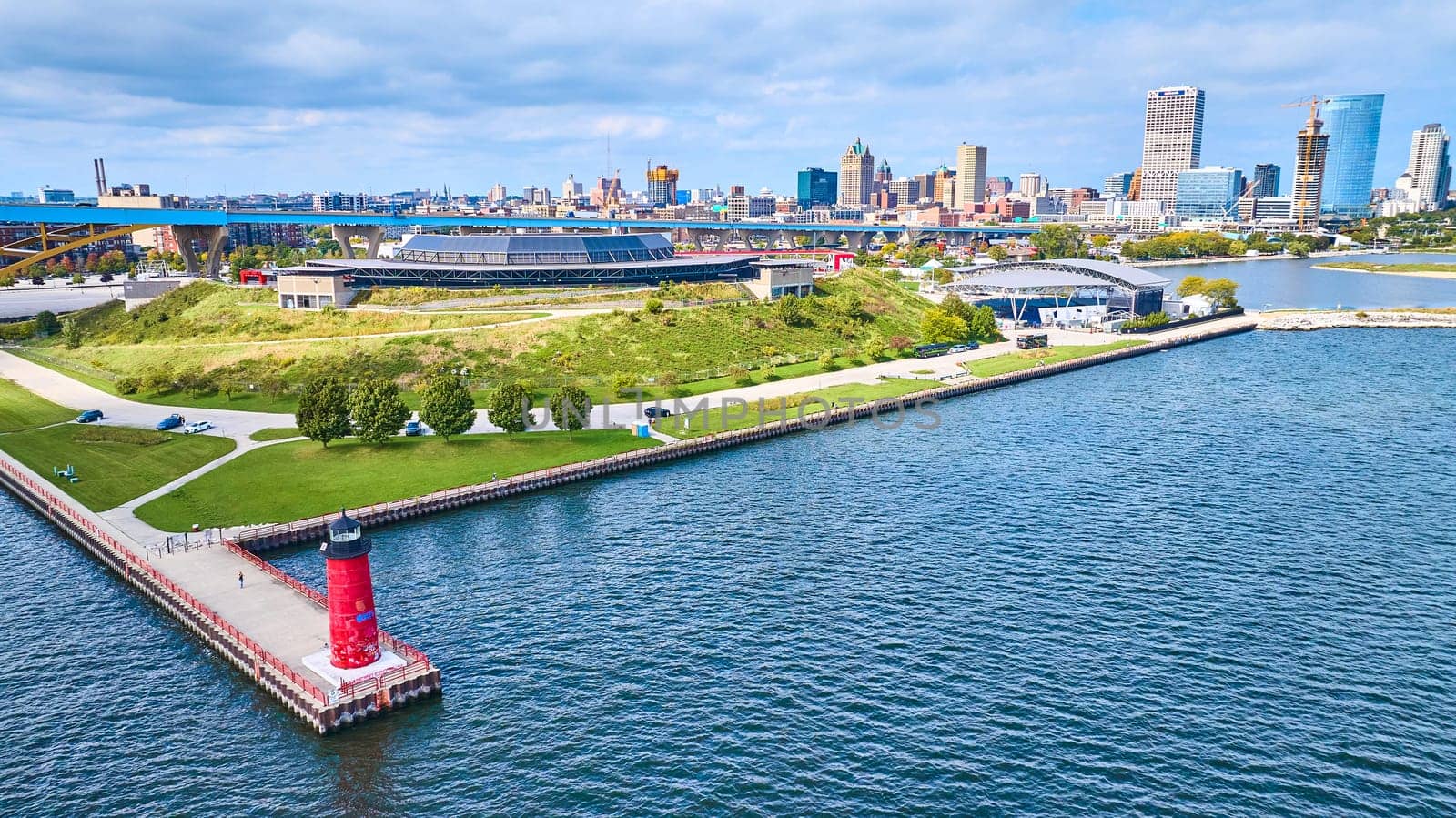 Aerial view of vibrant Milwaukee Pierhead Lighthouse guiding over Lake Michigan, with urban skyline and lush park in the backdrop