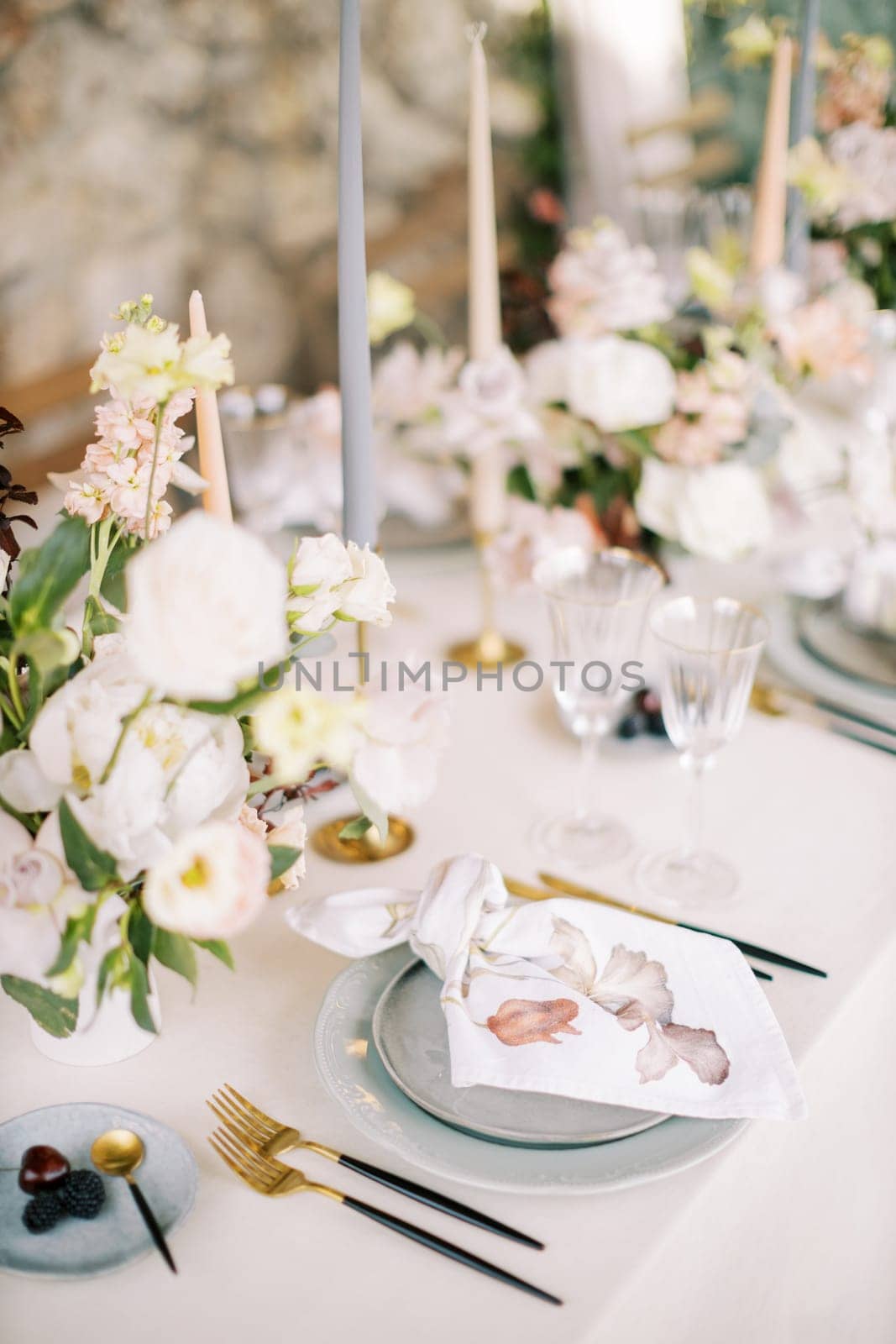 Knotted colorful napkin lies on a plate on the table next to a bouquet of flowers and cutlery by Nadtochiy