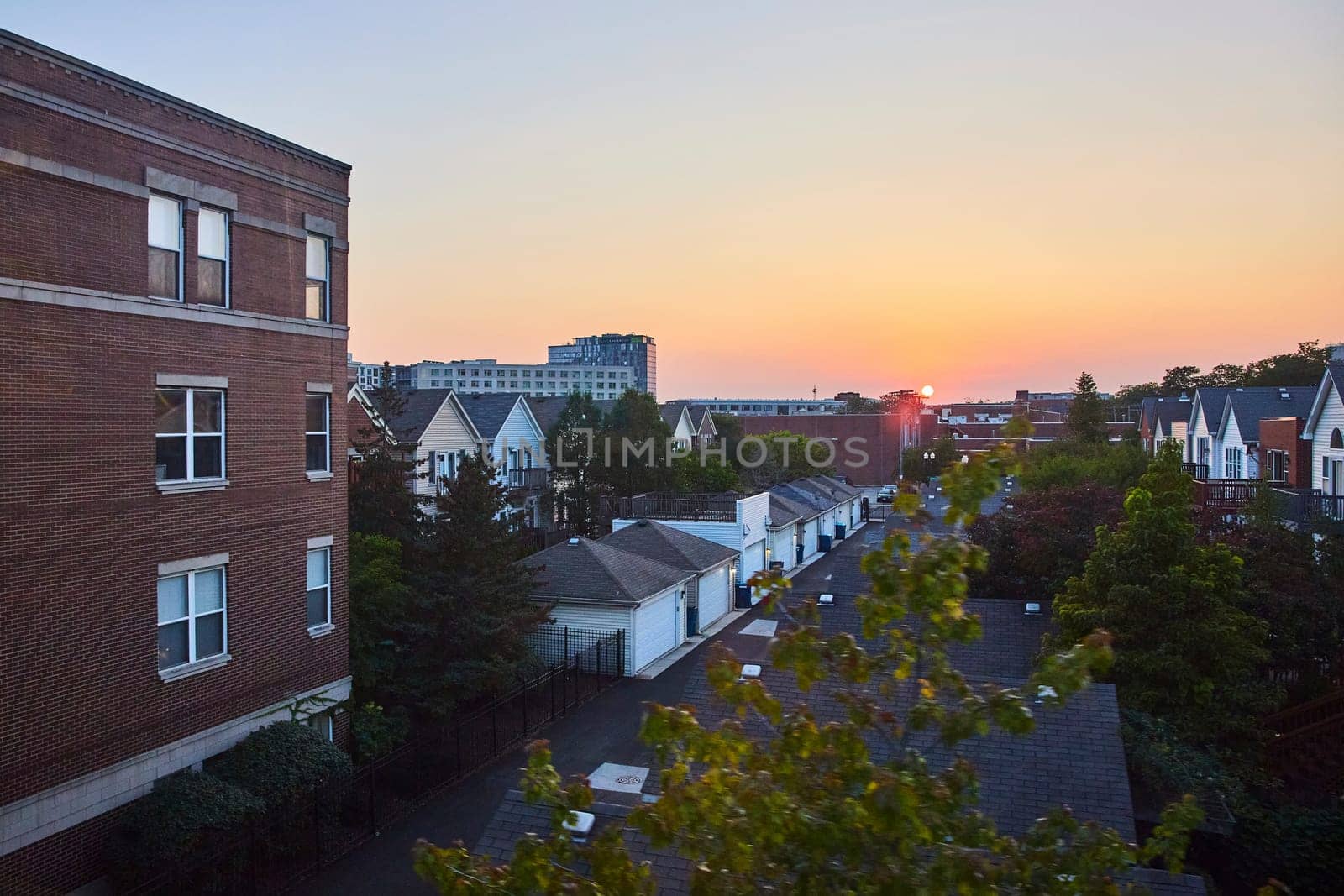 Image of Sun in distance rising over city buildings with rows of houses in Chicago, IL at sunset