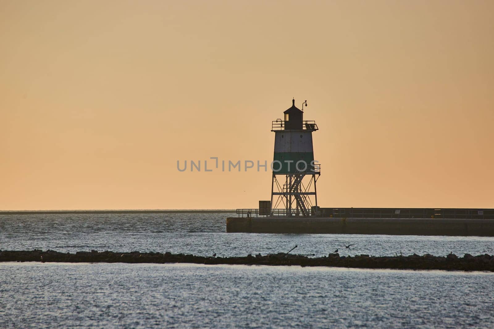 Image of Sunrise behind lighthouse at dawn with soft golden sky and Lake Michigan water in ocean endlessness