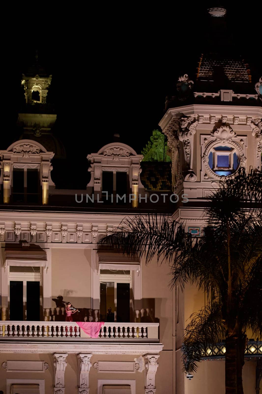 Monaco, Monte-Carlo, 12 November 2022: A girl plays the violin on the balcony of the famous Casino Monte-Carlo is at night, pink dress, attraction night illumination. High quality photo