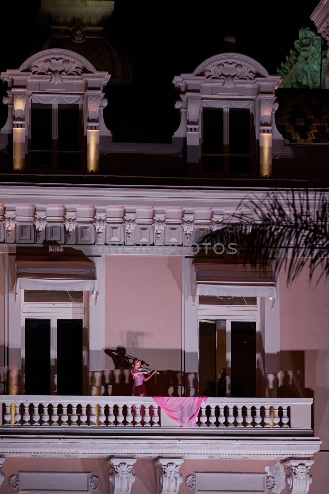 Monaco, Monte-Carlo, 12 November 2022: A girl plays the violin on the balcony of the famous Casino Monte-Carlo is at night, pink dress, attraction night illumination. High quality photo