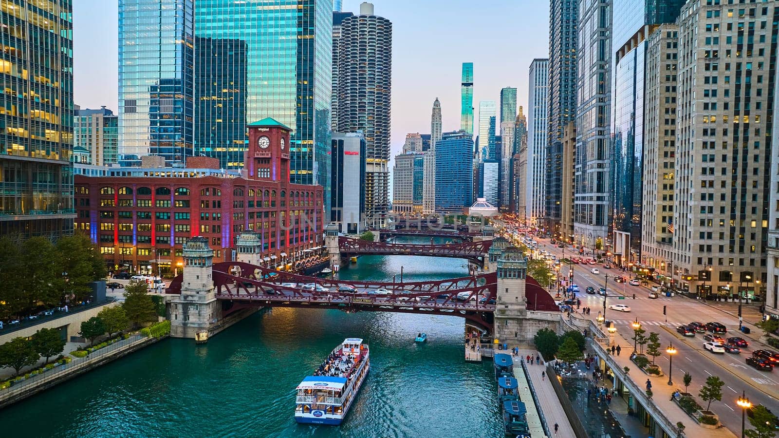 Image of Chicago boat going under canal bridge aerial with city lights and skyscrapers at blue hour, tourism