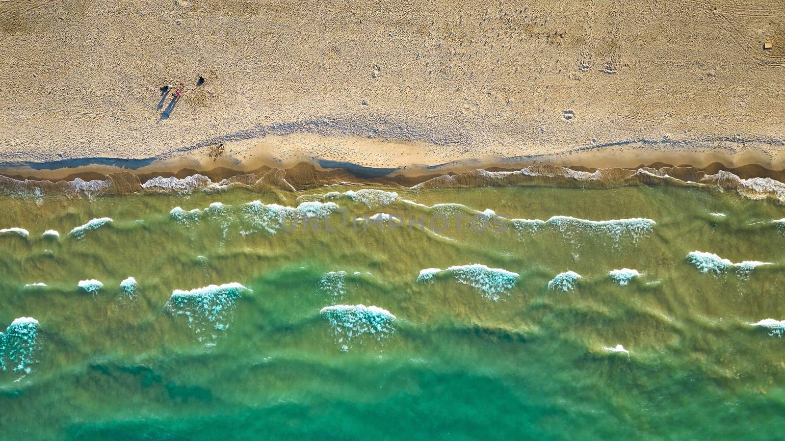 Aerial above green water waves on sunny day with beach along coast with tourists traveling on sand by njproductions