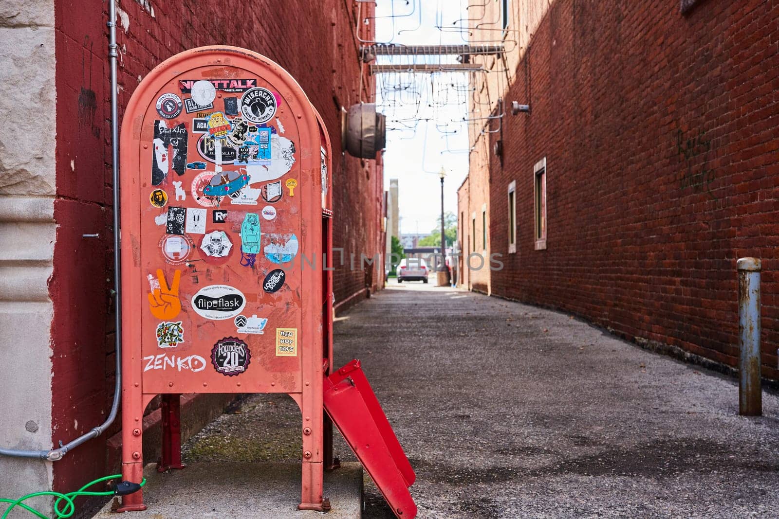 Daylight scene of weathered newspaper vending machine in a graffiti-adorned alleyway, Muncie, Indiana, 2023.